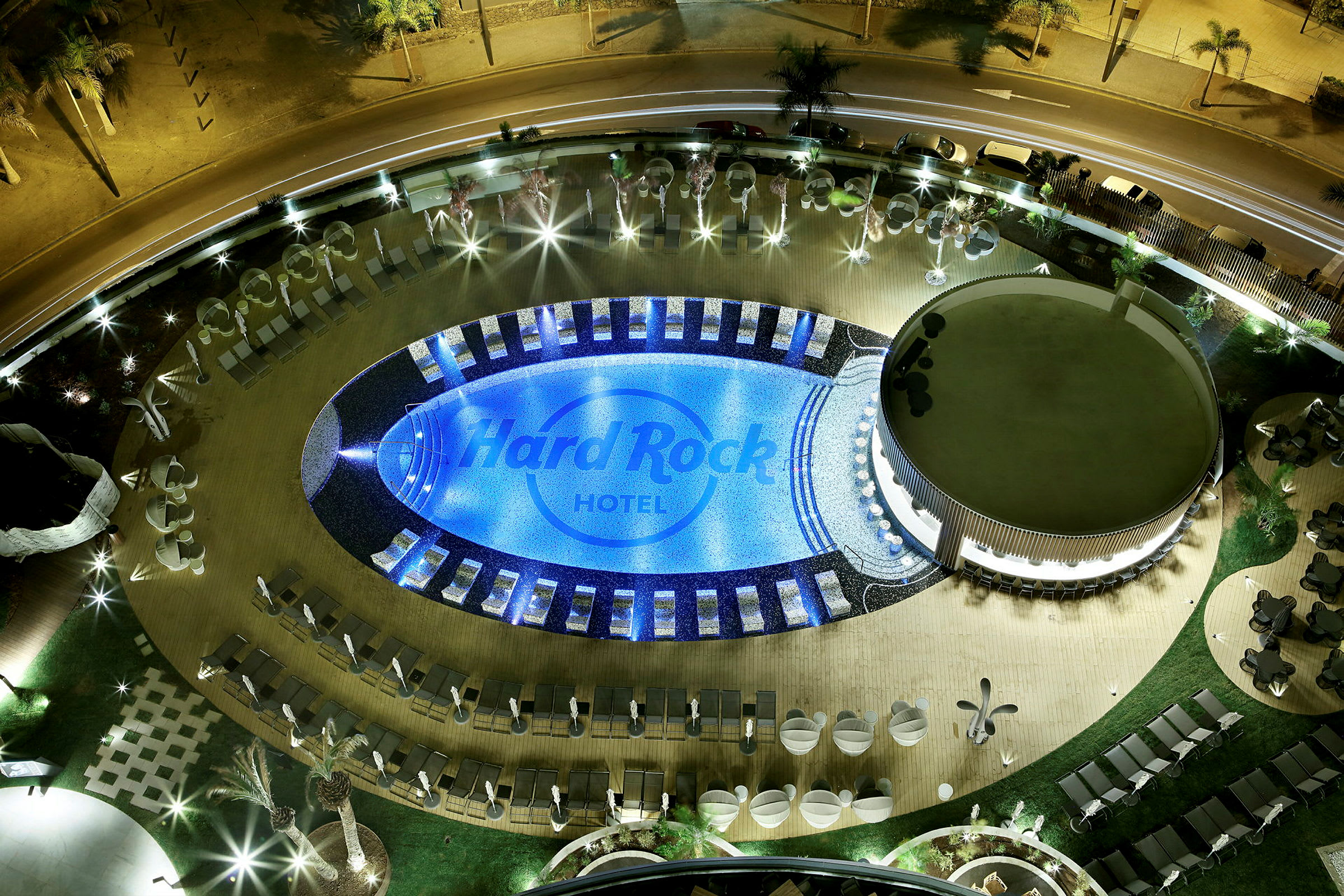 Luftfoto af en oplyst pool og det omkringliggende område ved Hard Rock Hotel om aftenen. (AI-genereret tekst)