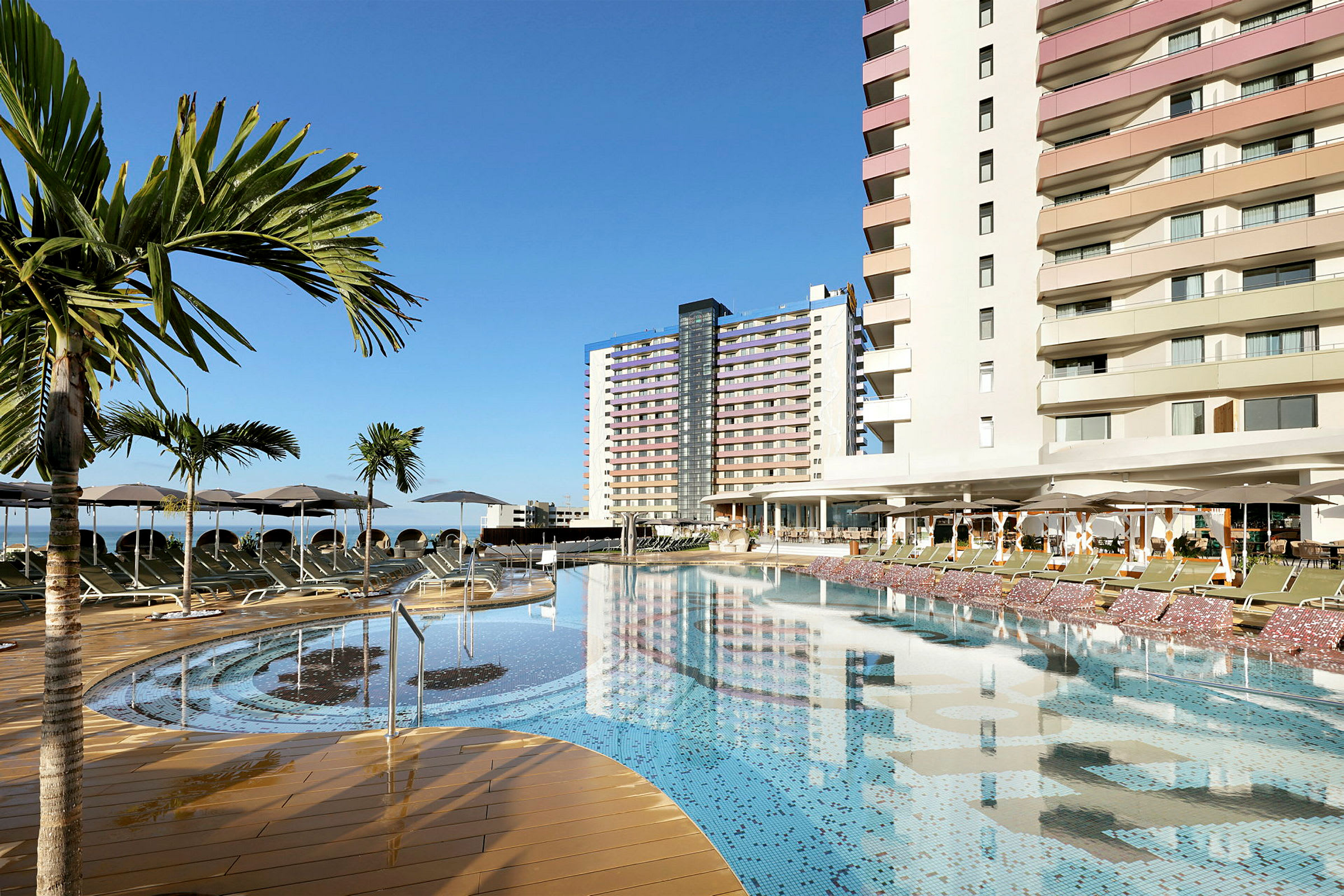 En udendørs pool ved et hotel med palmer og solstole. (AI-genereret tekst)