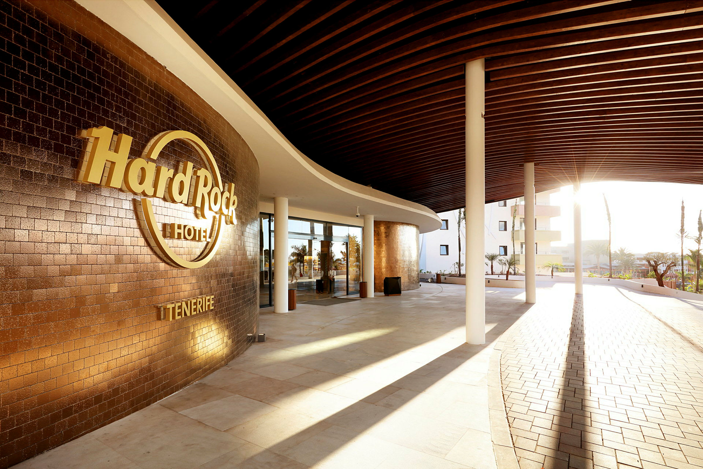 Indgangen til Hard Rock Hotel Tenerife med solskin og moderne design. (AI-genereret tekst)