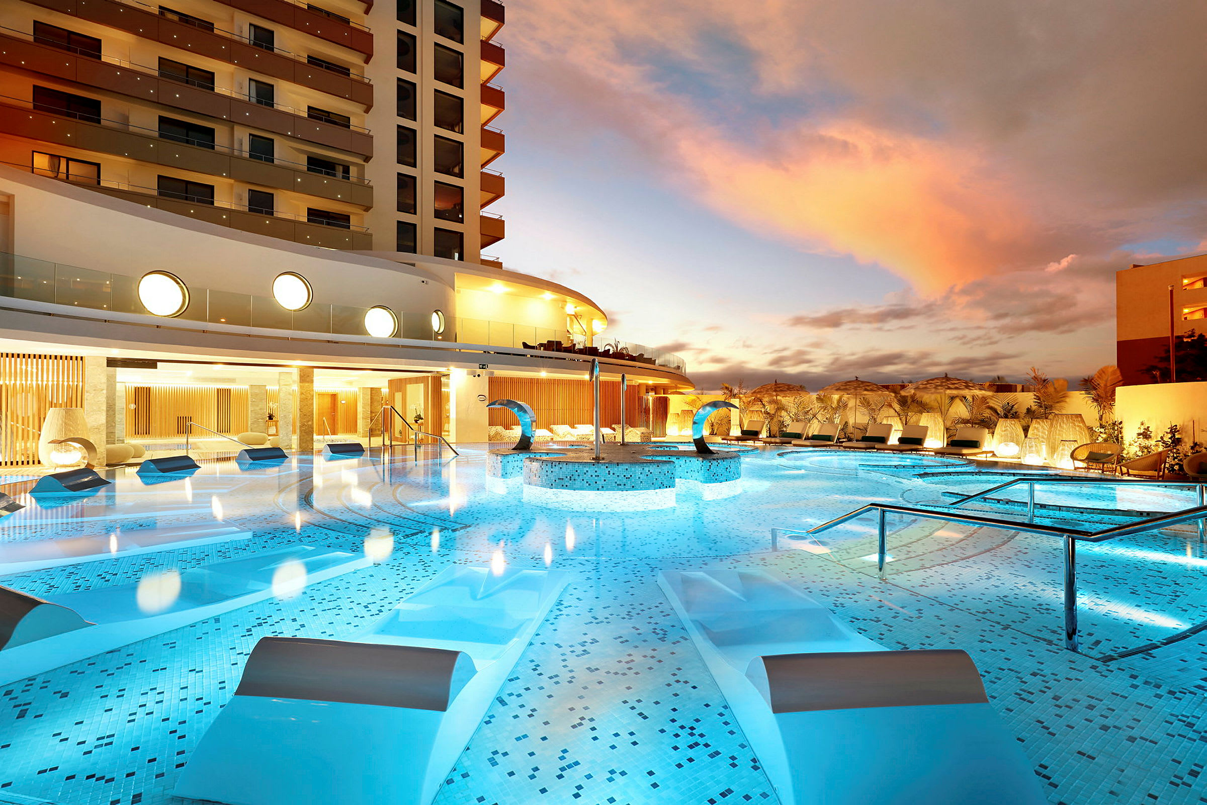 En luksuriøs pool i et hotelområde med moderne arkitektur og liggestole ved skumring. (AI-genereret tekst)