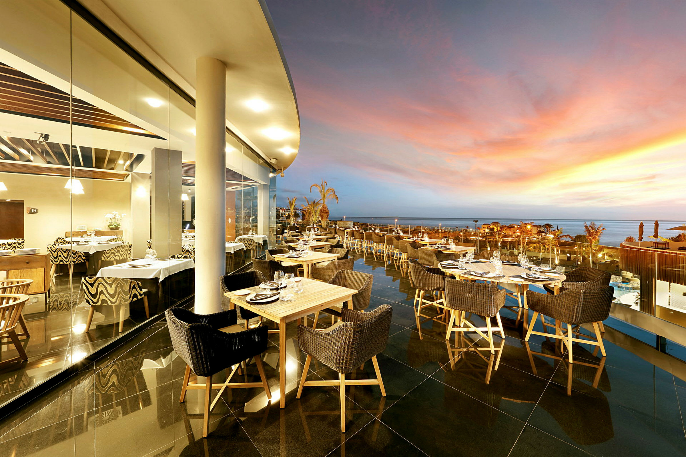 Udendørsrestaurant med udsigt over havet under solnedgang. (AI-genereret tekst)