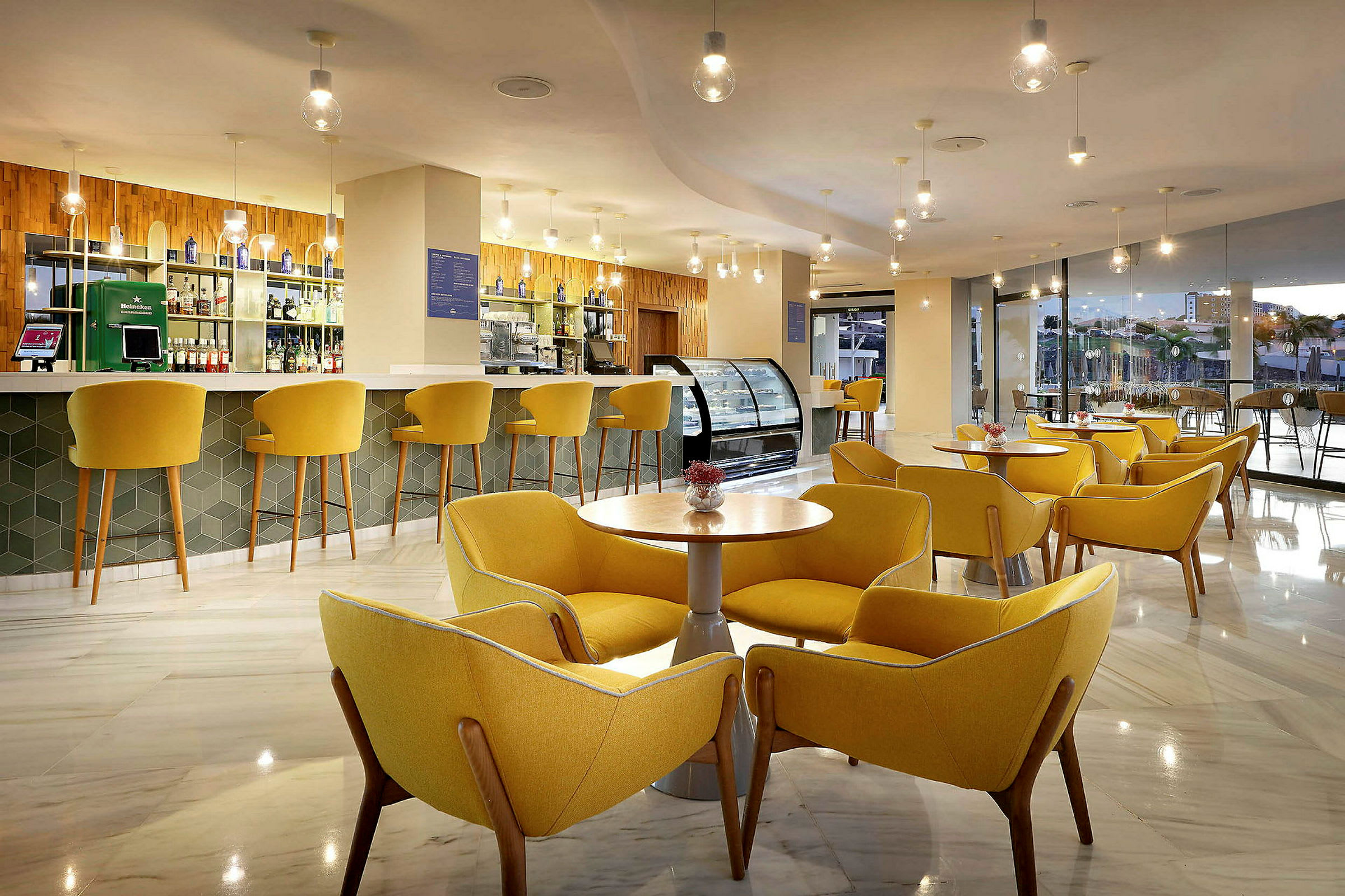 En moderne lounge med gule stole og borde samt en bar i baggrunden. (AI-genereret tekst)