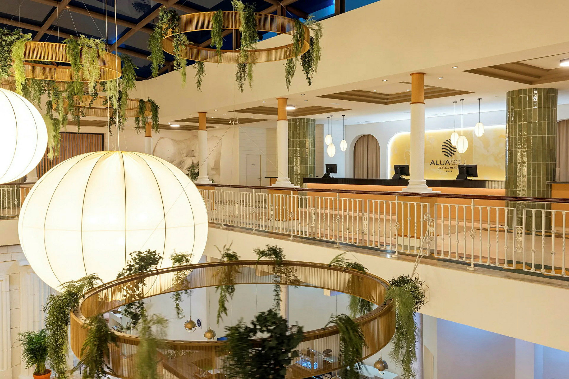 Interiør af en hotellobby med store lysekroner, hængende plantepynt og receptionen synlig. (AI-genereret tekst)
