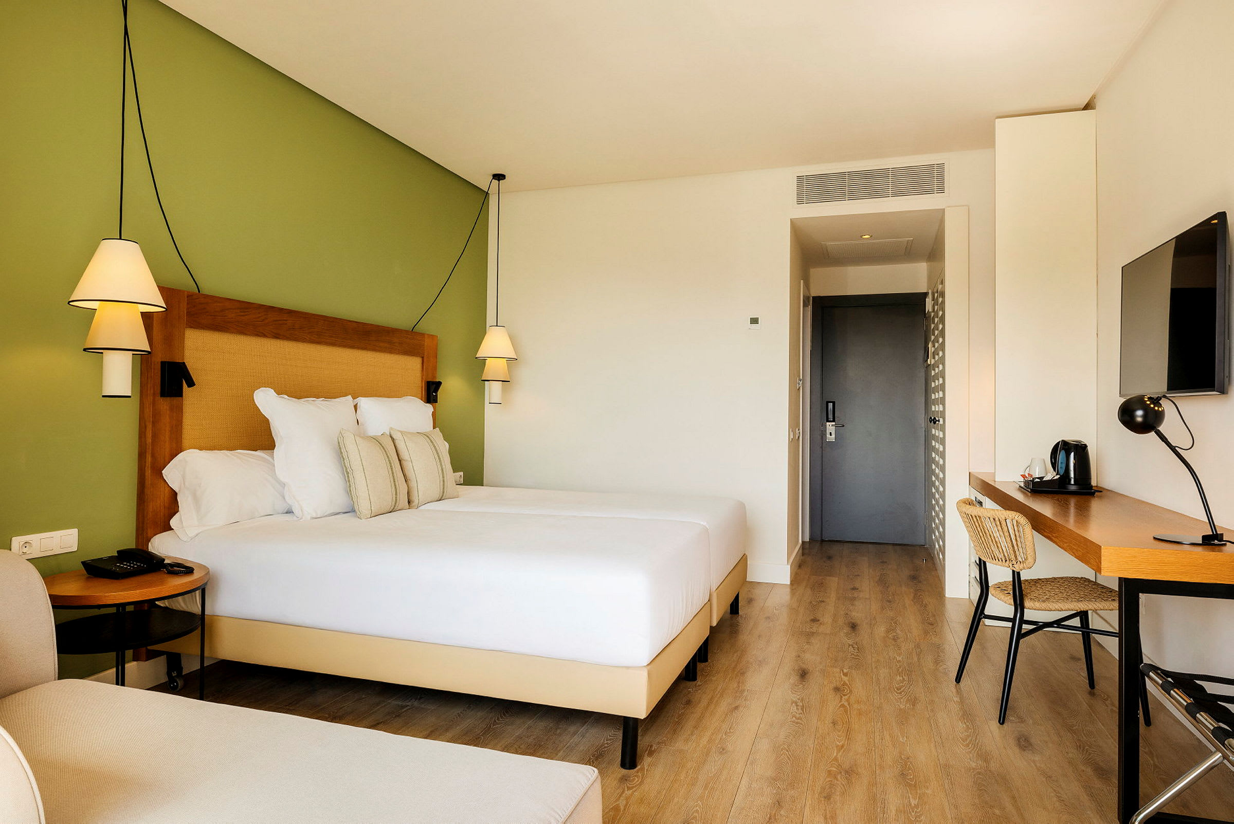 Hotelværelse med en bred seng, skrivebord og grøn væg. (AI-genereret tekst)