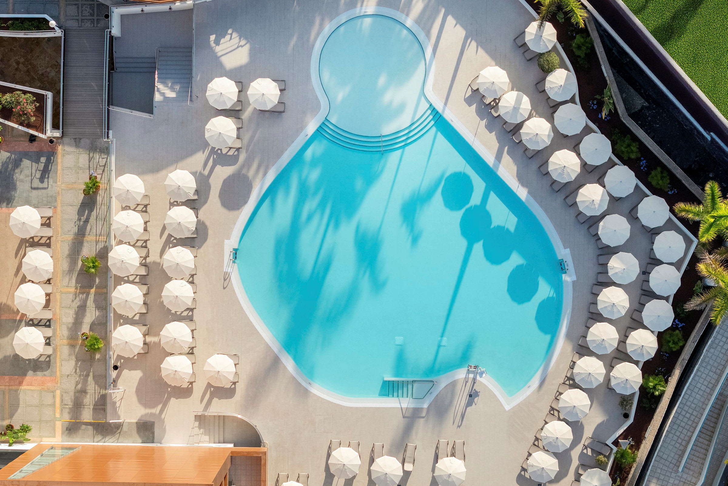 Luftfoto af en pool omgivet af liggestole og parasoller. (AI-genereret tekst)
