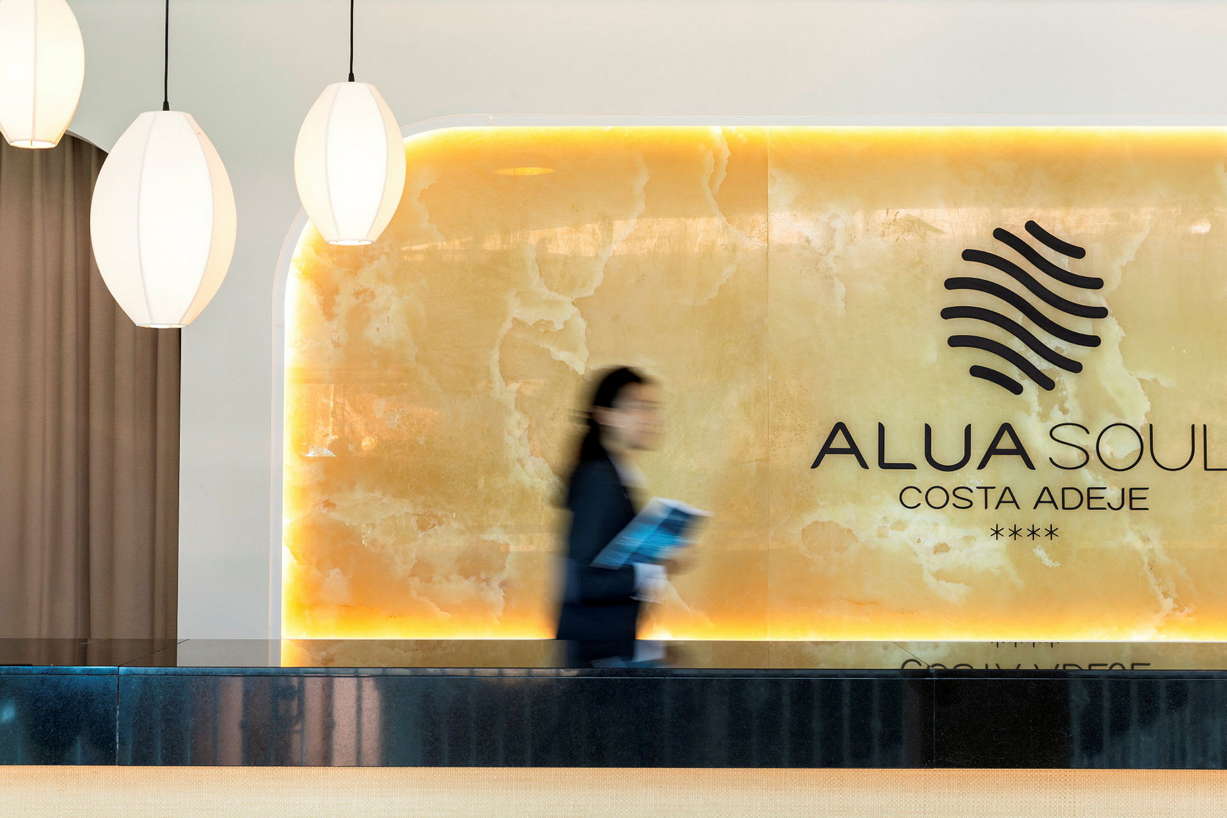 Receptionen på Alua Soul Costa Adeje vises med lyse detaljer og en person i bevægelse. (AI-genereret tekst)