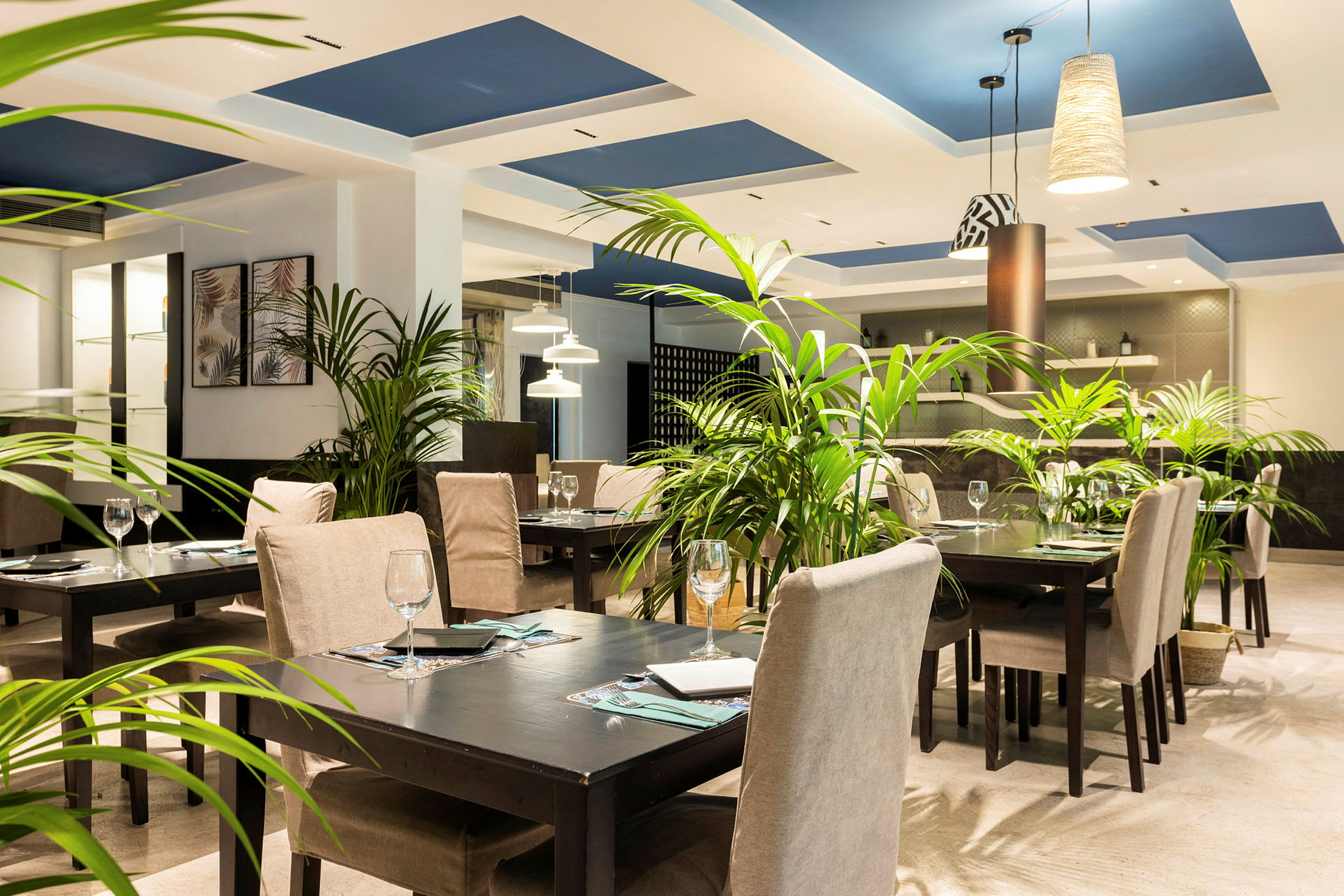 En restaurant med dækkede borde, grønne planter og moderne belysning. (AI-genereret tekst)