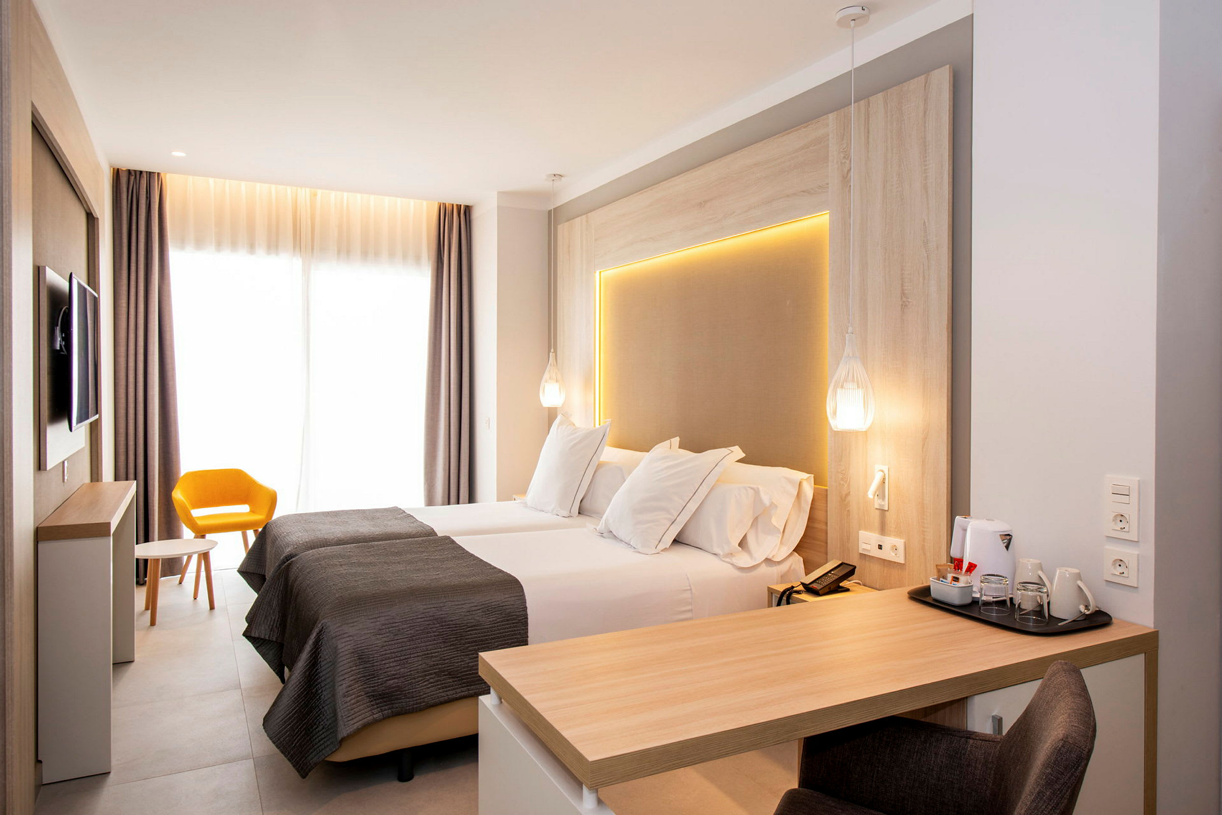 Moderne hotelværelse med to enkeltsenge, skrivebord og gul stol. (AI-genereret tekst)