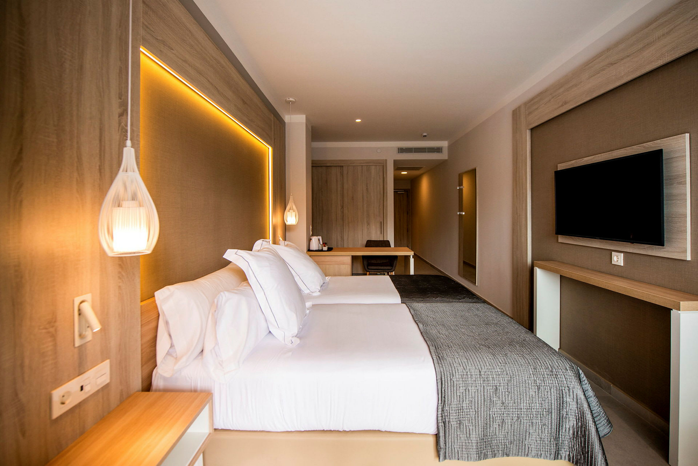 Hotelværelse med dobbeltseng, vægmonteret tv og skrivebord. (AI-genereret tekst)