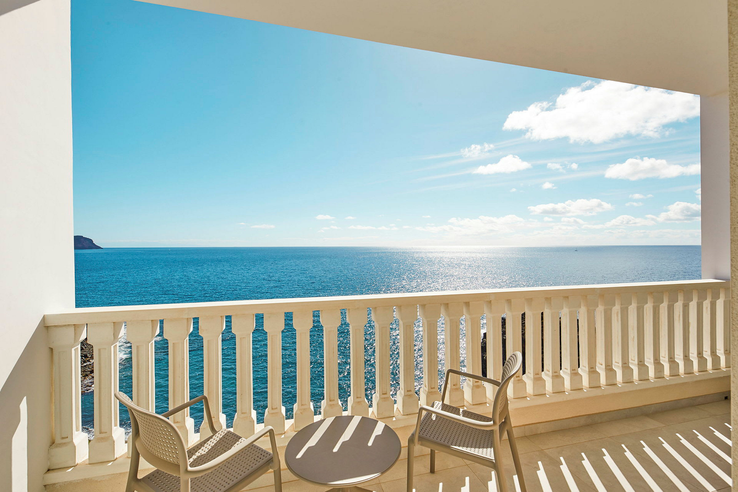 Udsigt fra en balkon med bord og stole mod havet. (AI-genereret tekst)