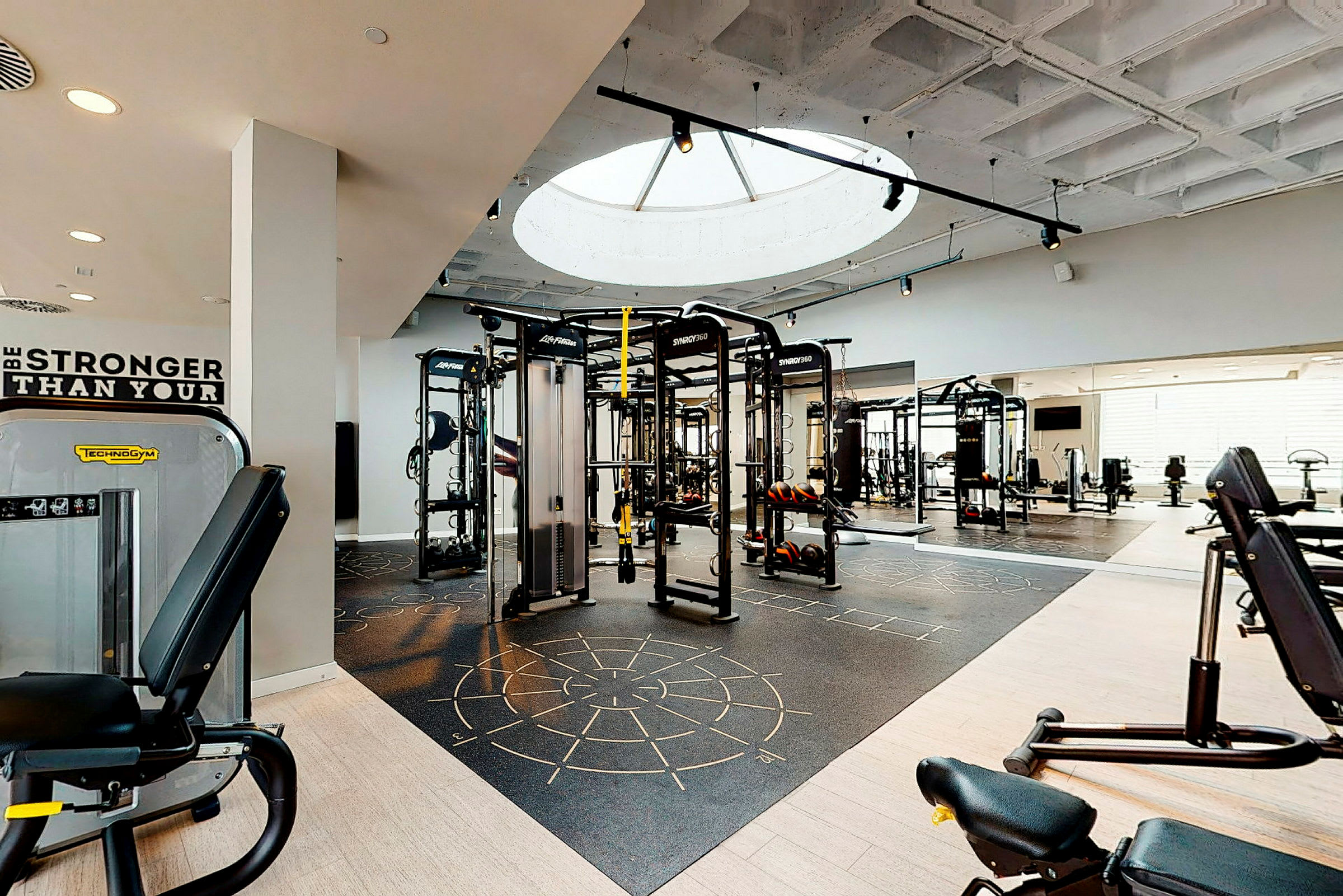 Et moderne fitnesscenter med træningsmaskiner og frie vægte samt et ovenlysvindue, der lukker dagslys ind. (AI-genereret tekst)