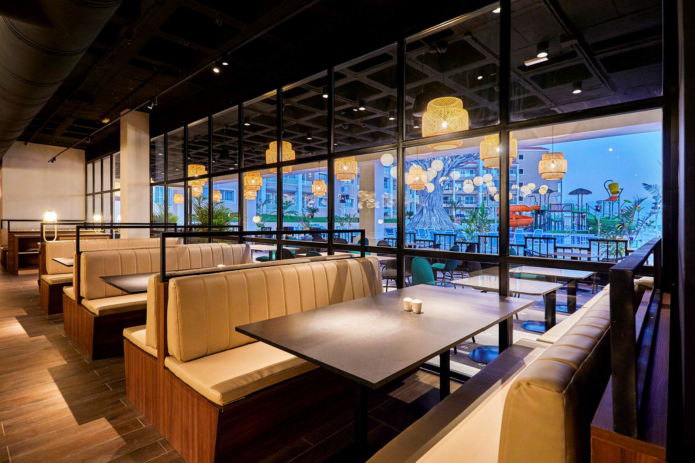 En moderne restaurant med lyse bænke og store vinduer, der vender ud mod en terrasse med pool og dekorationer. (AI-genereret tekst)