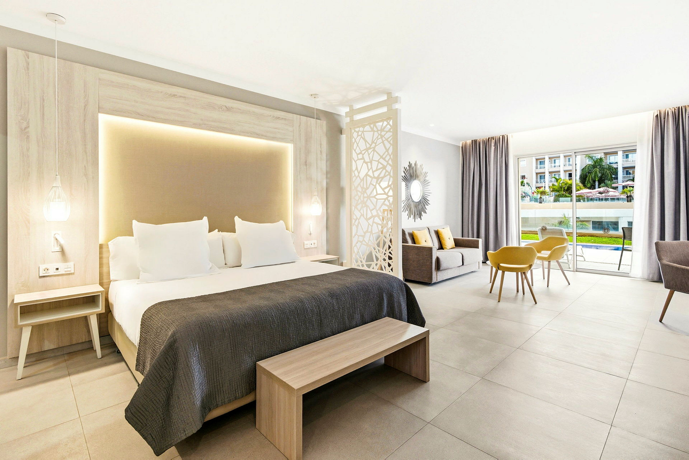 Et moderne hotelværelse med en dobbeltseng, siddeområde og udsigt over poolområdet gennem store glasdøre. (AI-genereret tekst)