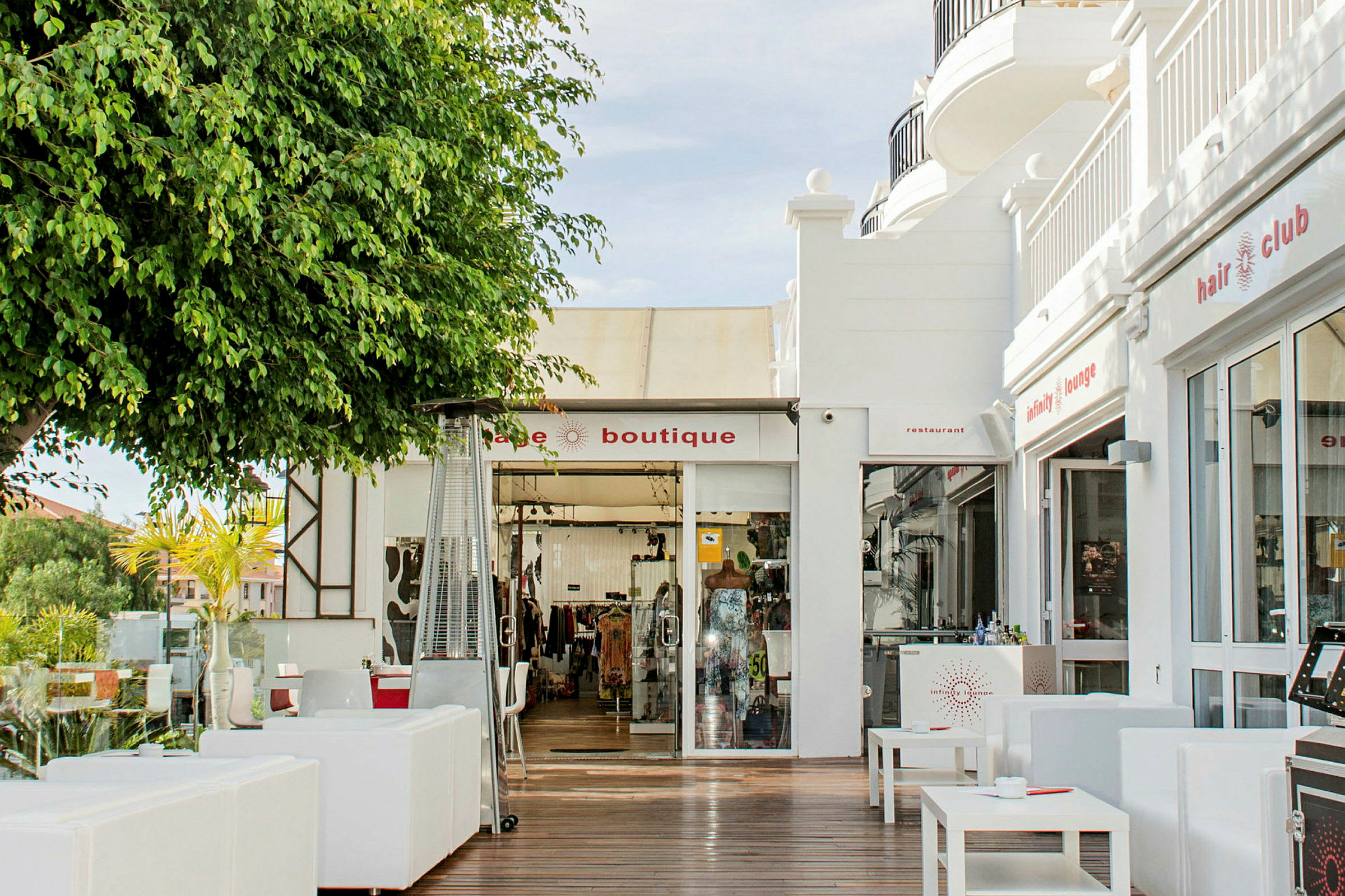 Billede af en butik og restaurant med udendørs møbler i et solrigt miljø. (AI-genereret tekst)