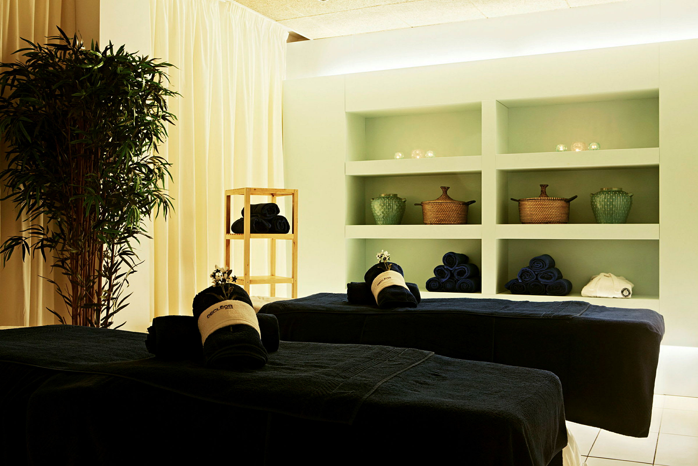 Et spa-rum med massageborde, håndklæder og dekorationer. (AI-genereret tekst)