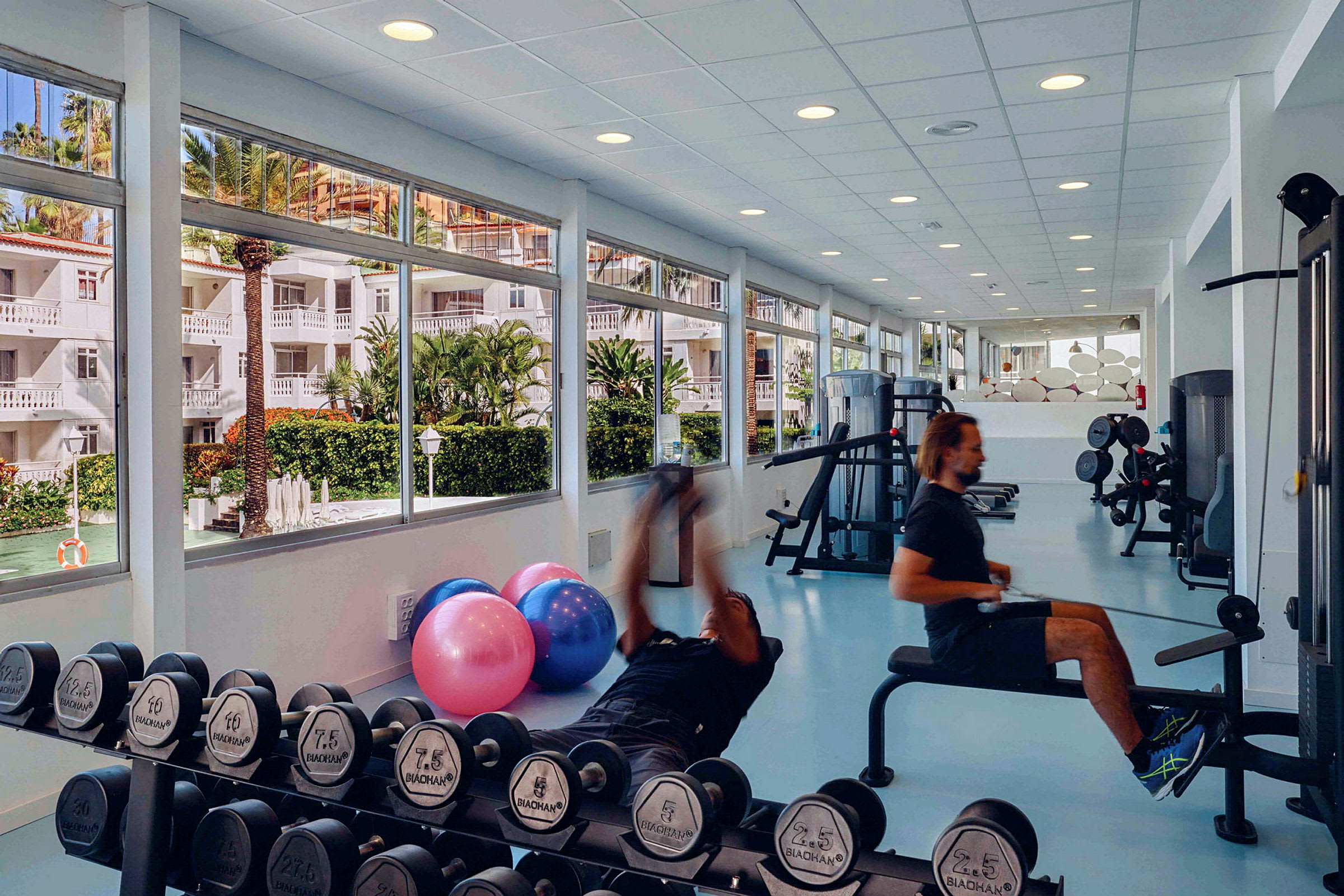 Fitnessrum med træningsudstyr og store vinduer med udsigt. (AI-genereret tekst)