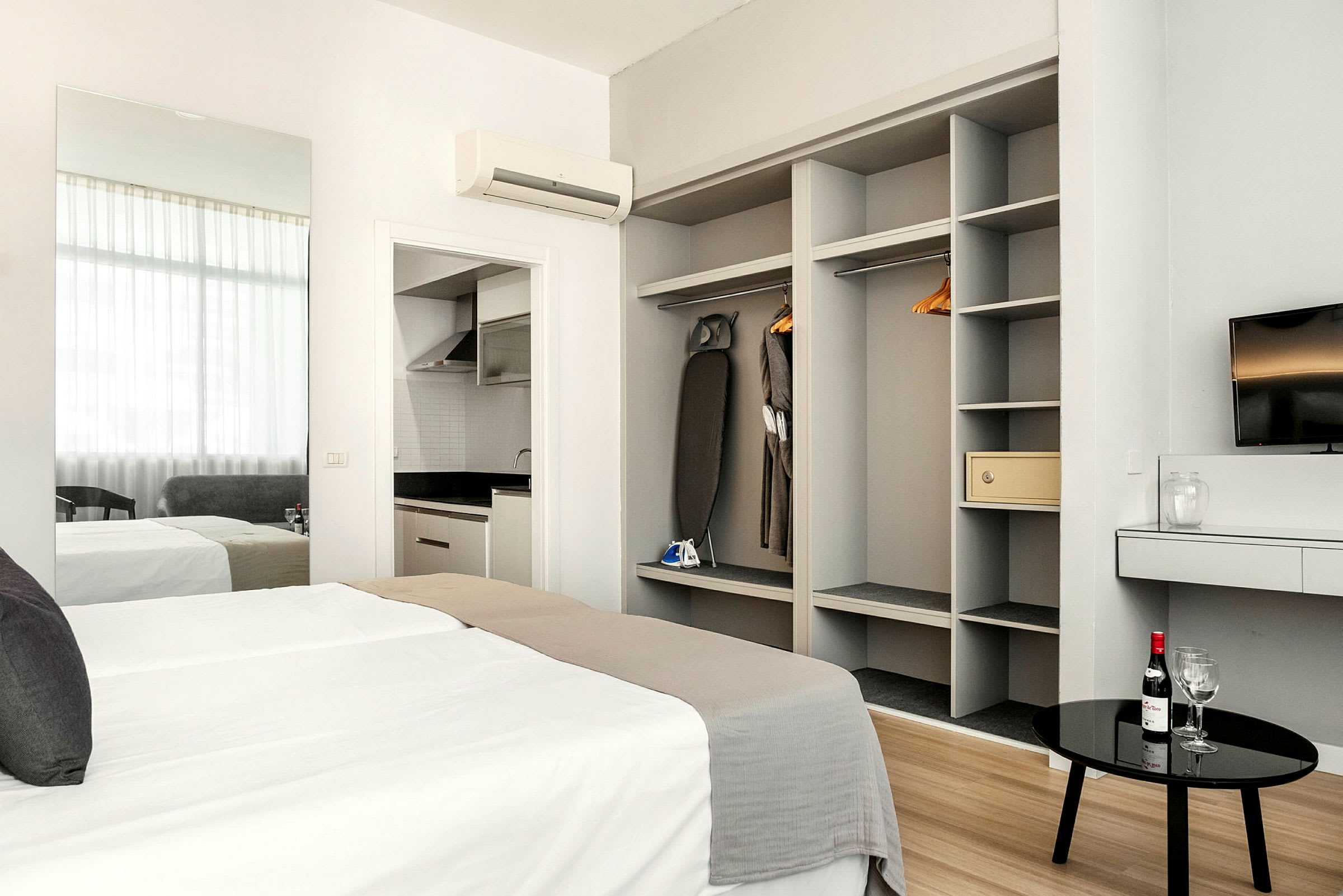 Moderne hotelværelse med seng, garderobe, et TV og køkkenområde. (AI-genereret tekst)