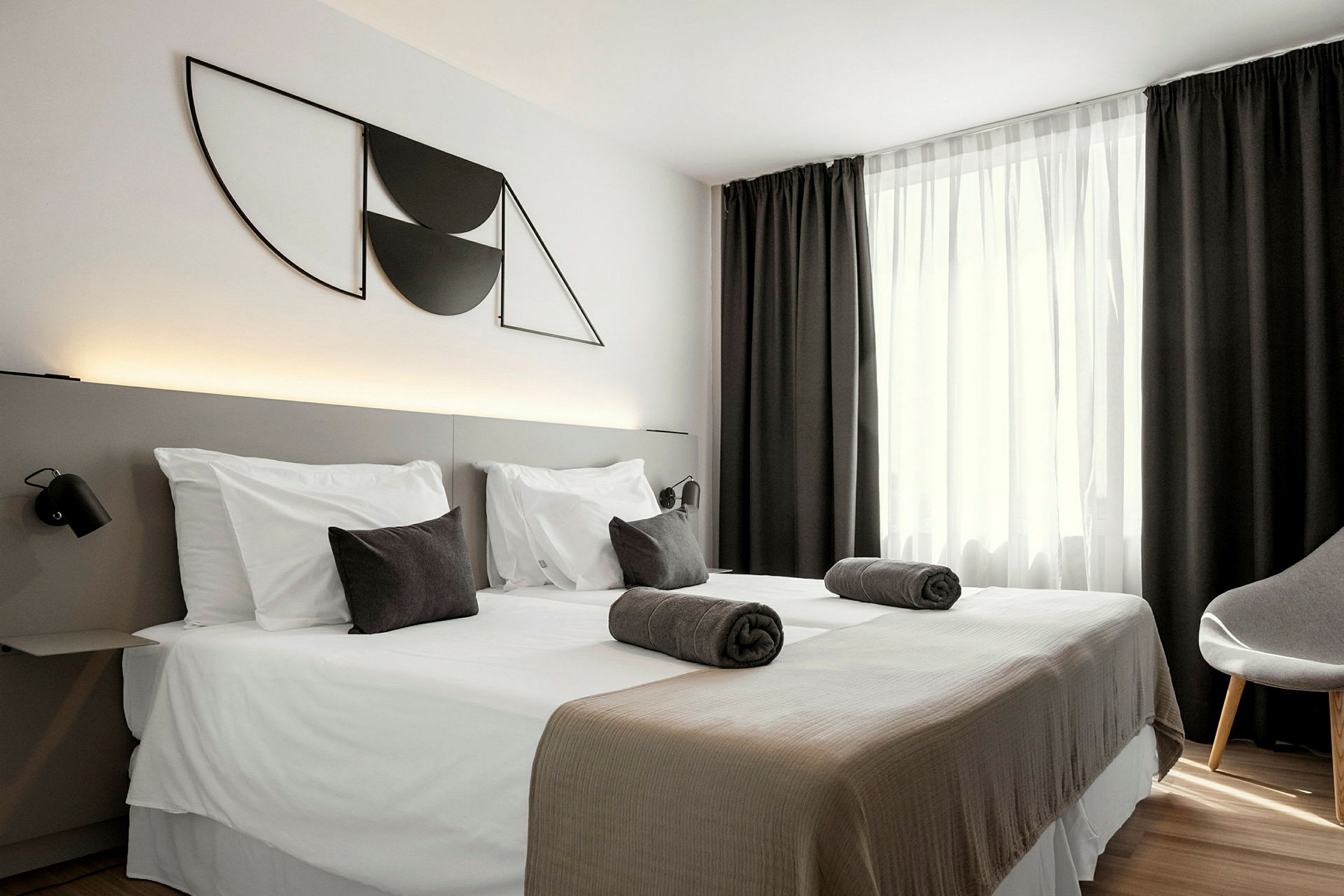 Et hotelværelse med to enkeltsenge, mørke gardiner og moderne vægdekoration. (AI-genereret tekst)