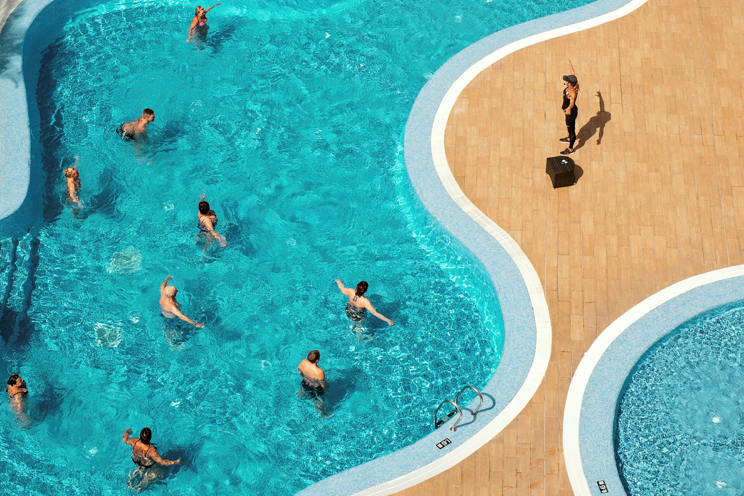 En pool med personer, der dyrker vand-aerobic under ledelse af en instruktør. (AI-genereret tekst)