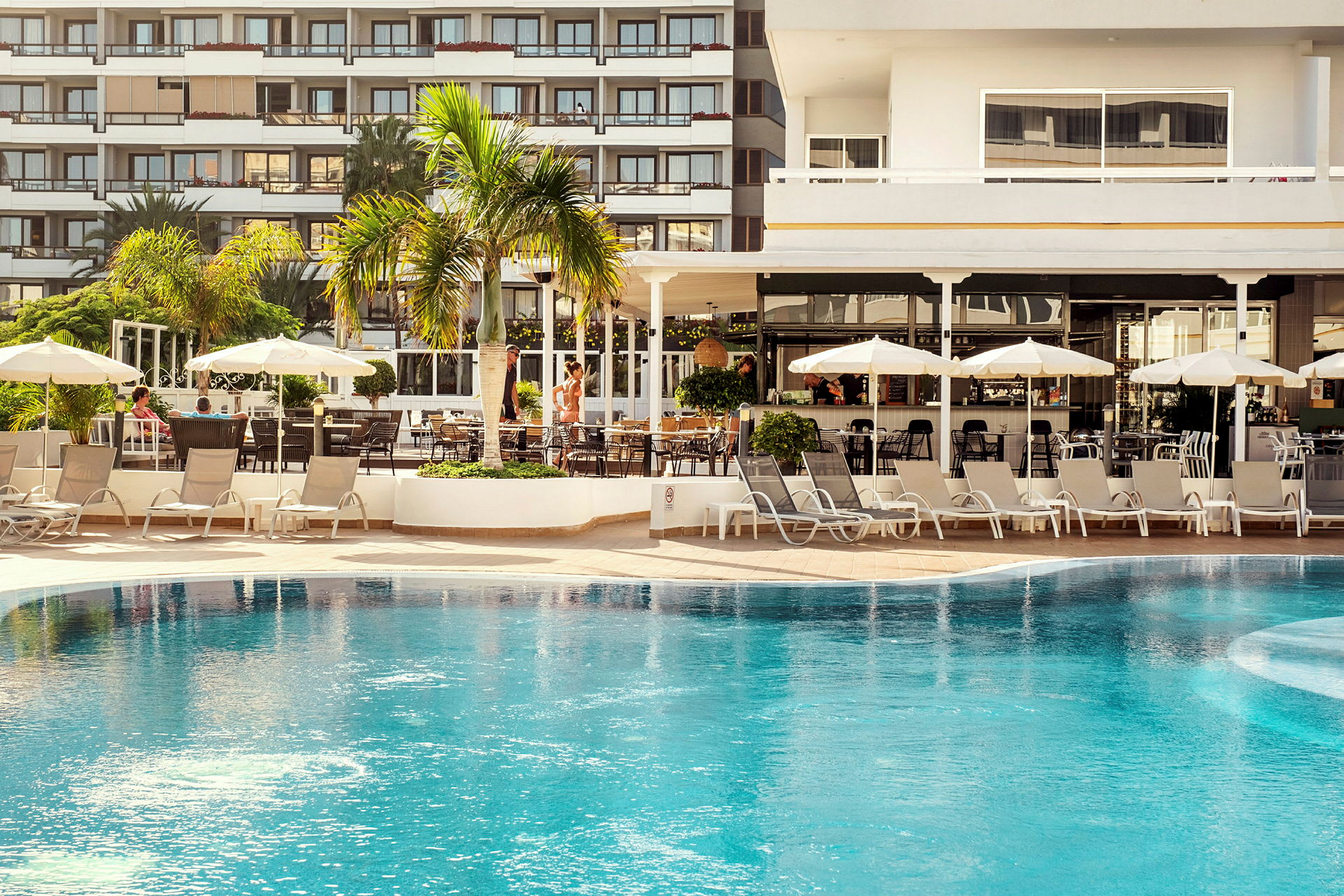 Billede af en hotelpool tæt på et område med liggestole og parasoller. (AI-genereret tekst)