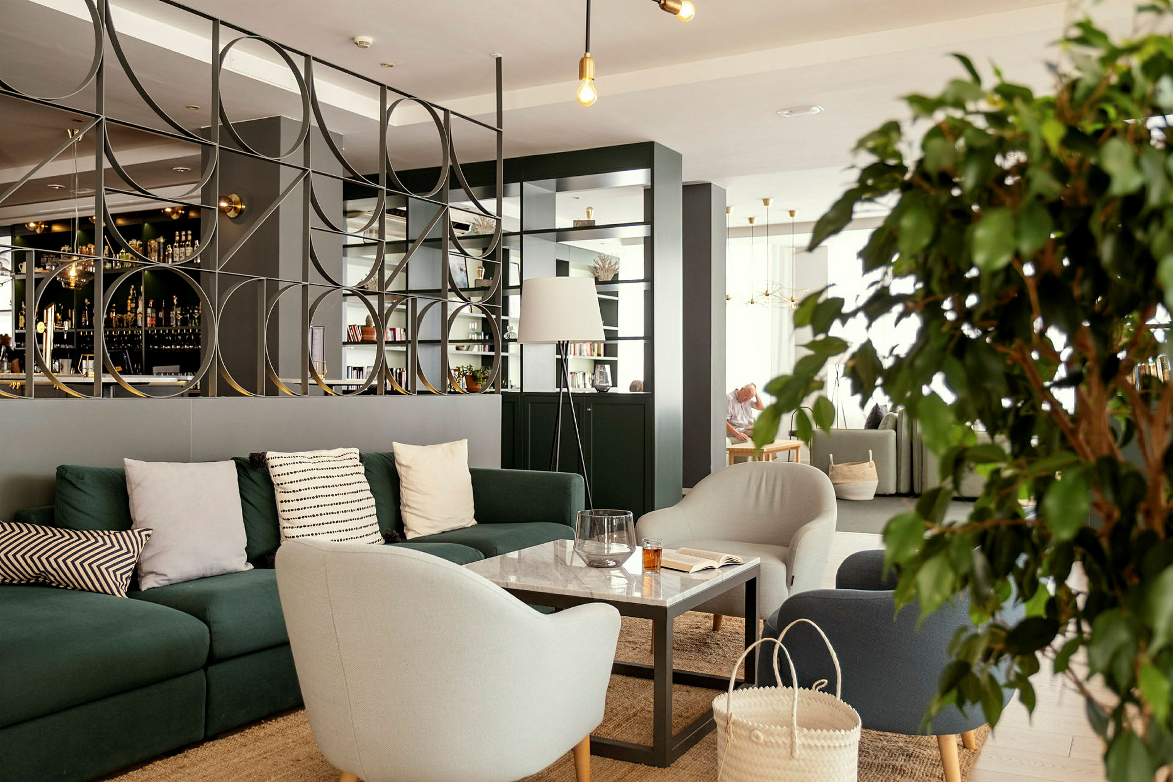 En moderne lounge med sofaer, lænestole og et bord foran en dekorativ skillevæg. (AI-genereret tekst)