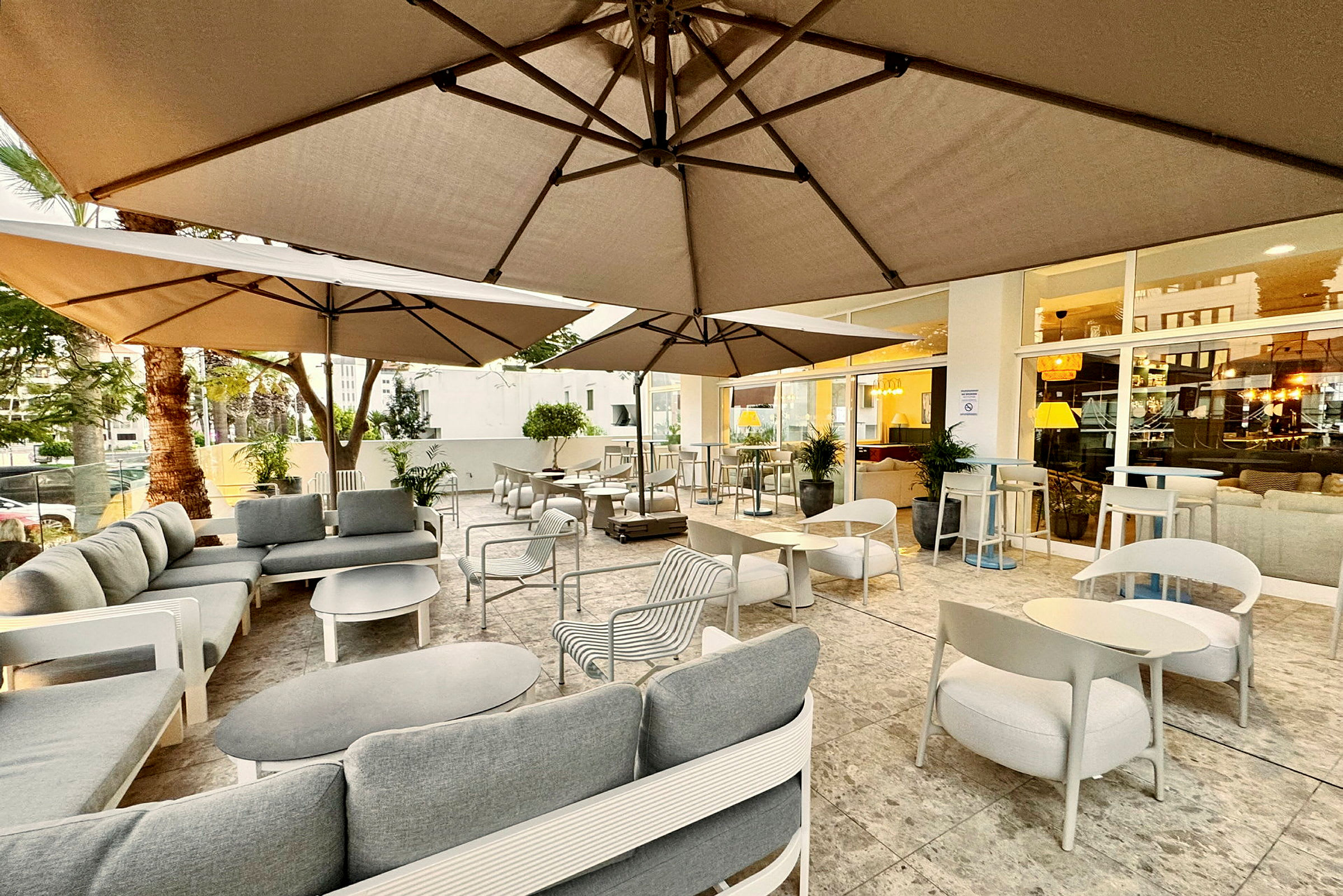 Udendørs serveringsområde med sofaer og borde under parasoller. (AI-genereret tekst)