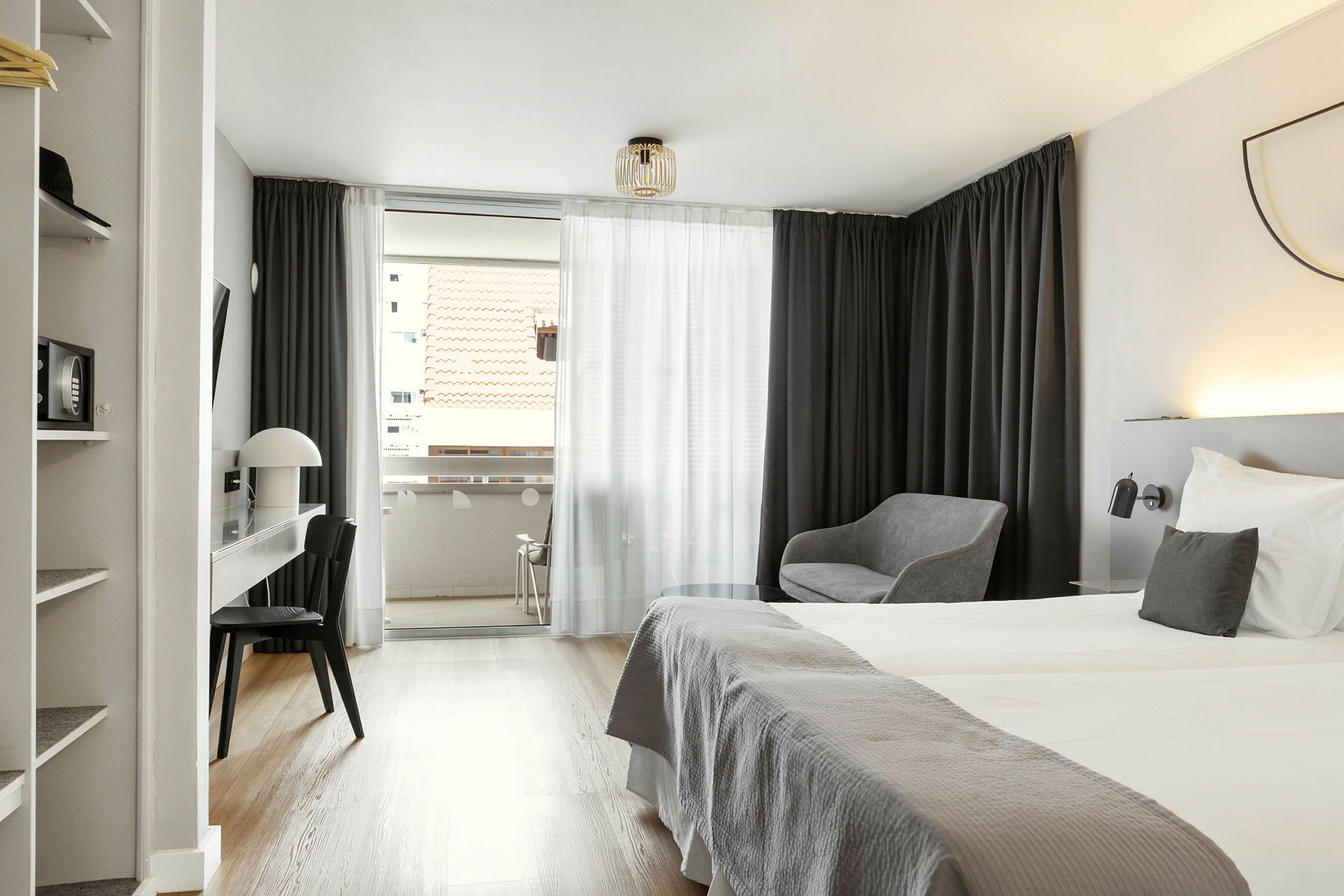 Et hotelværelse med dobbeltseng, skrivebord, stol og siddeområde; udsigt til en altan med tagudsigt. (AI-genereret tekst)