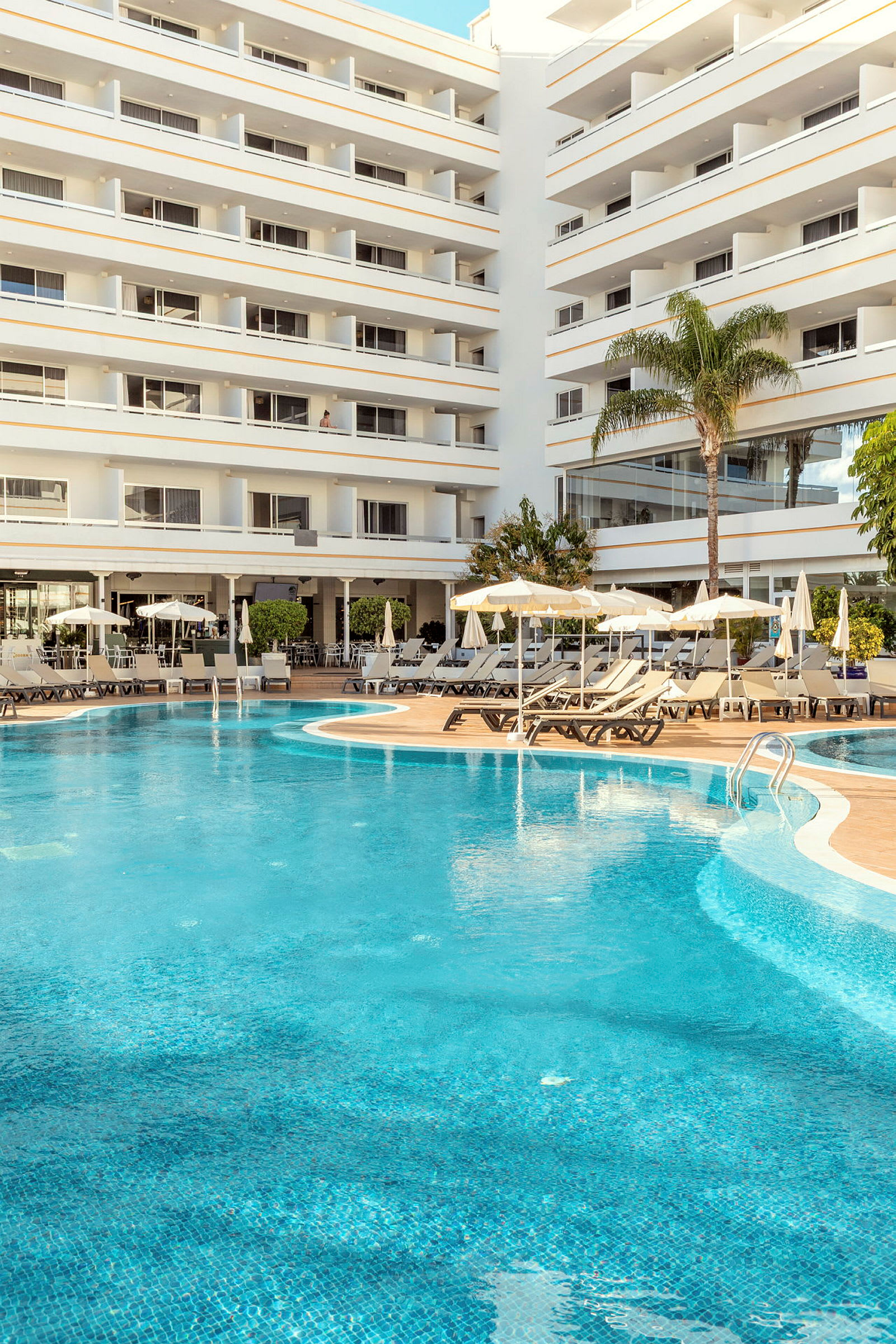 Poolområde foran et hotel med flere etager. (AI-genereret tekst)