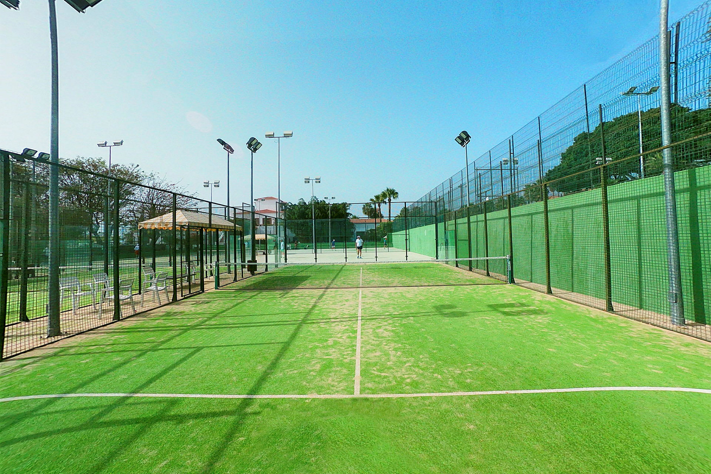 En grøn padelbane med net og belysning, omkranset af hegn. (AI-genereret tekst)