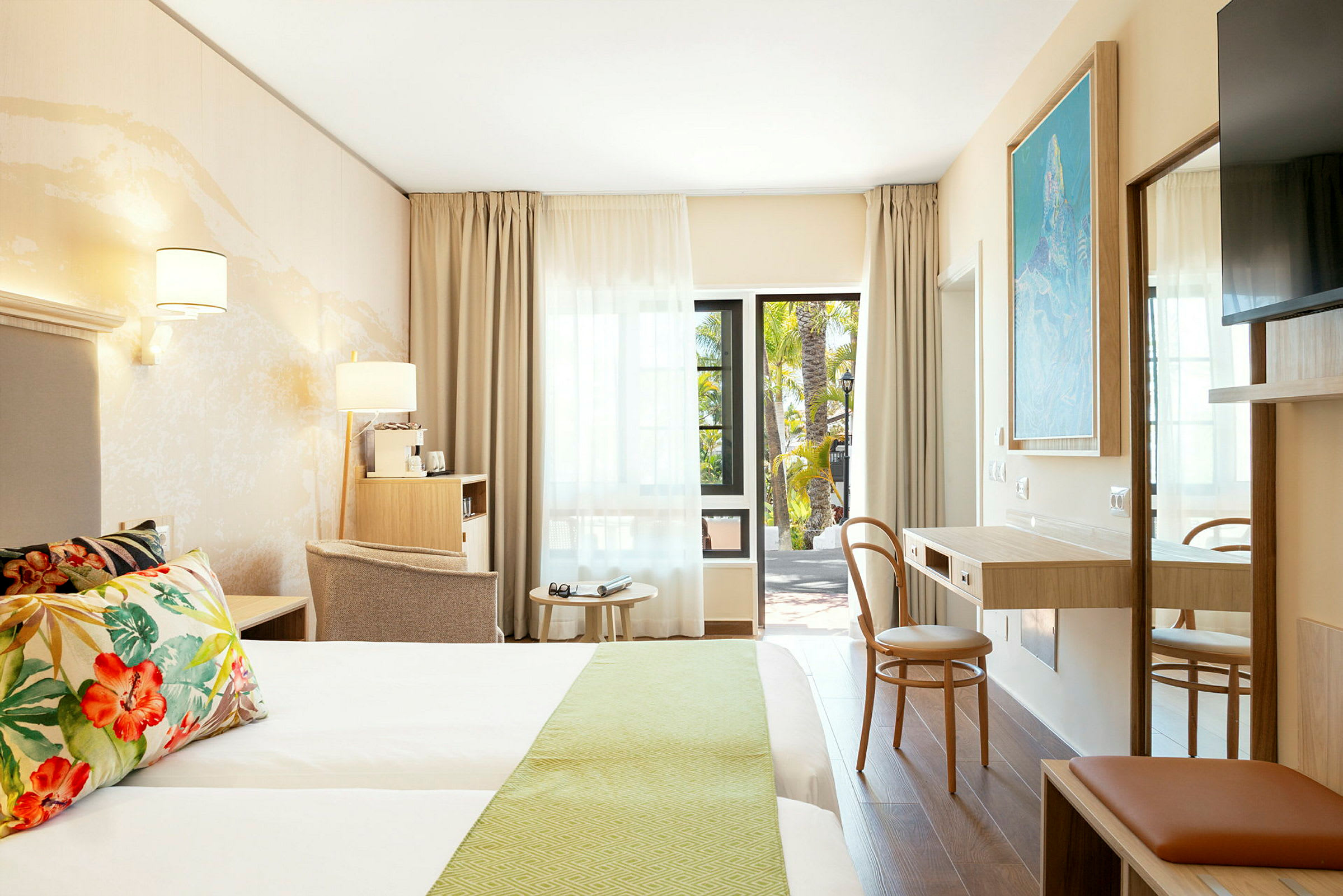 Billede af et moderne hotelværelse med dobbeltseng, skrivebord og siddepladser, samt en åben dør mod en balkon. (AI-genereret tekst)
