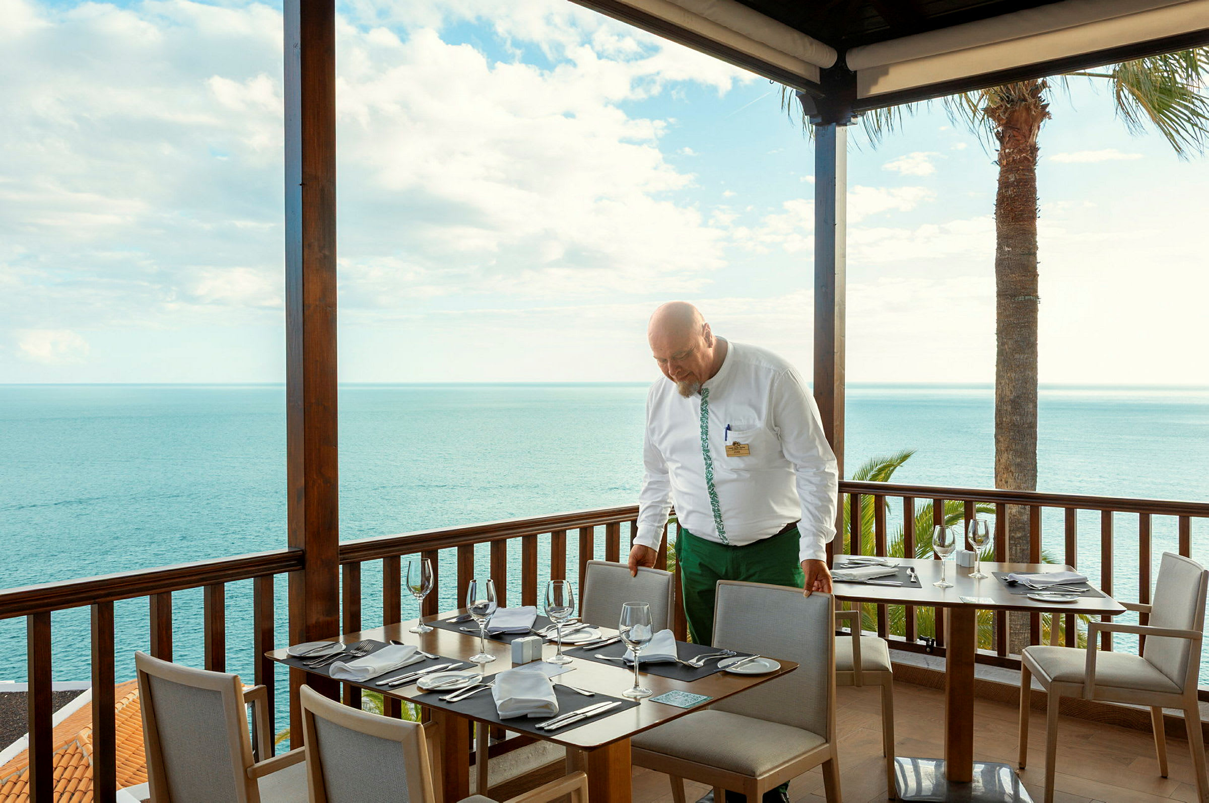 En spiseplads med dækkede borde på en terrasse med udsigt over havet. (AI-genereret tekst)