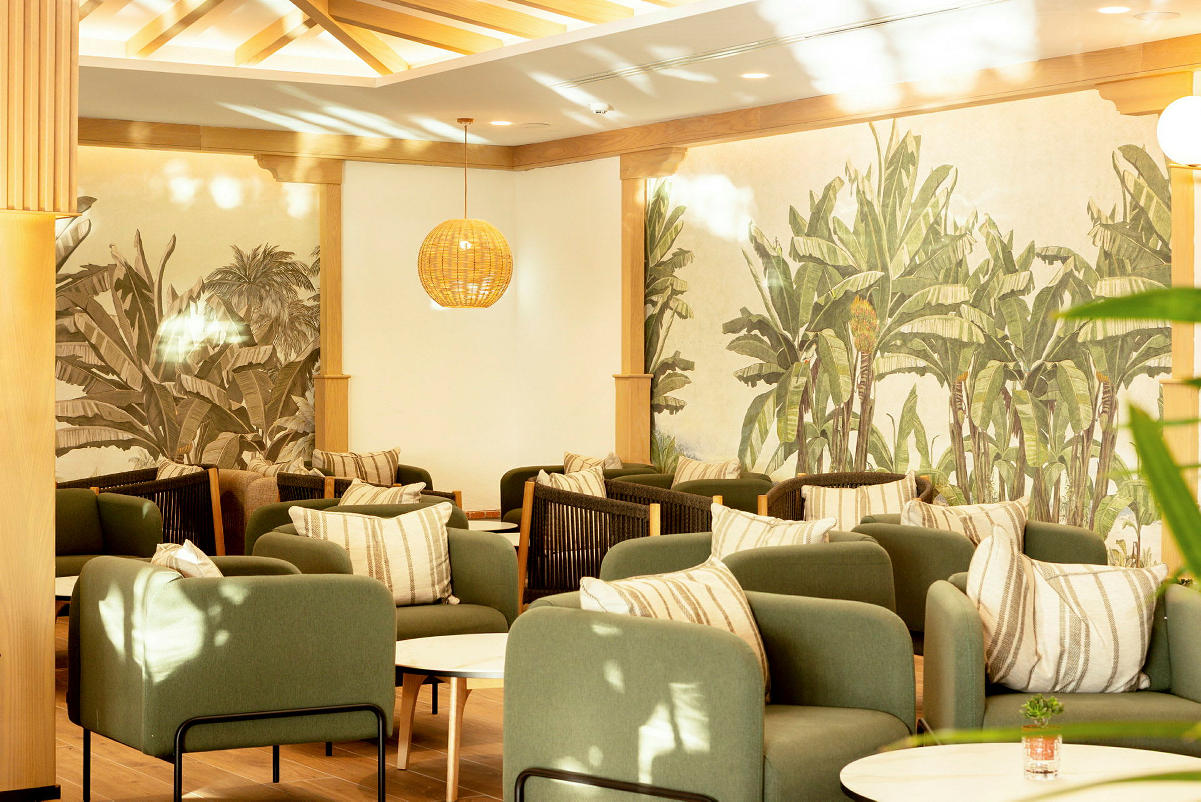 En elegant lounge med grønne lænestole, stribede puder og vægge pyntet med plantemotiver. (AI-genereret tekst)