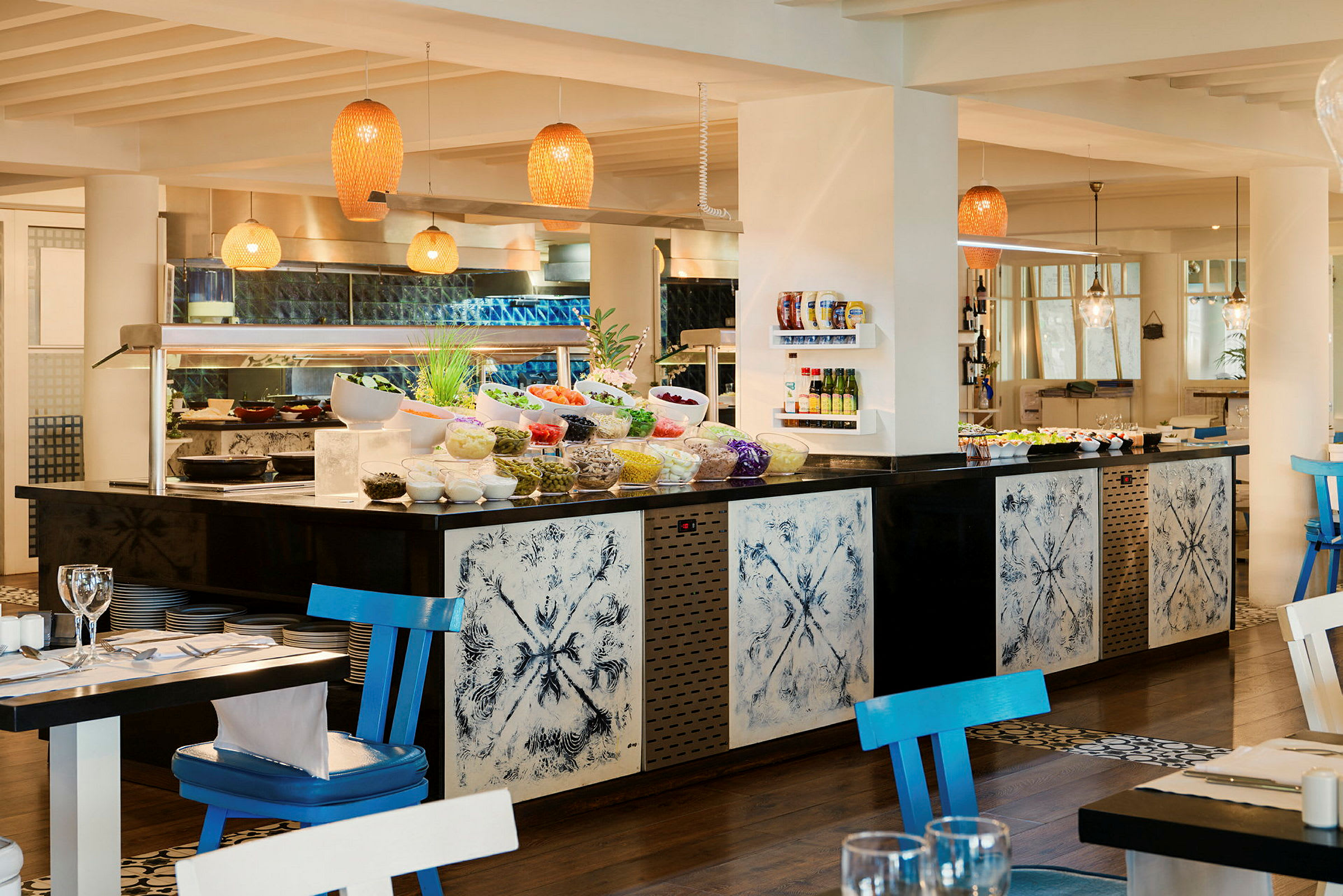 Et billede af en buffet i en restaurant med lys og åben indretning. Farverig mad og skåle med forskellige retter er anbragt foran dekorative paneler. (AI-genereret tekst)