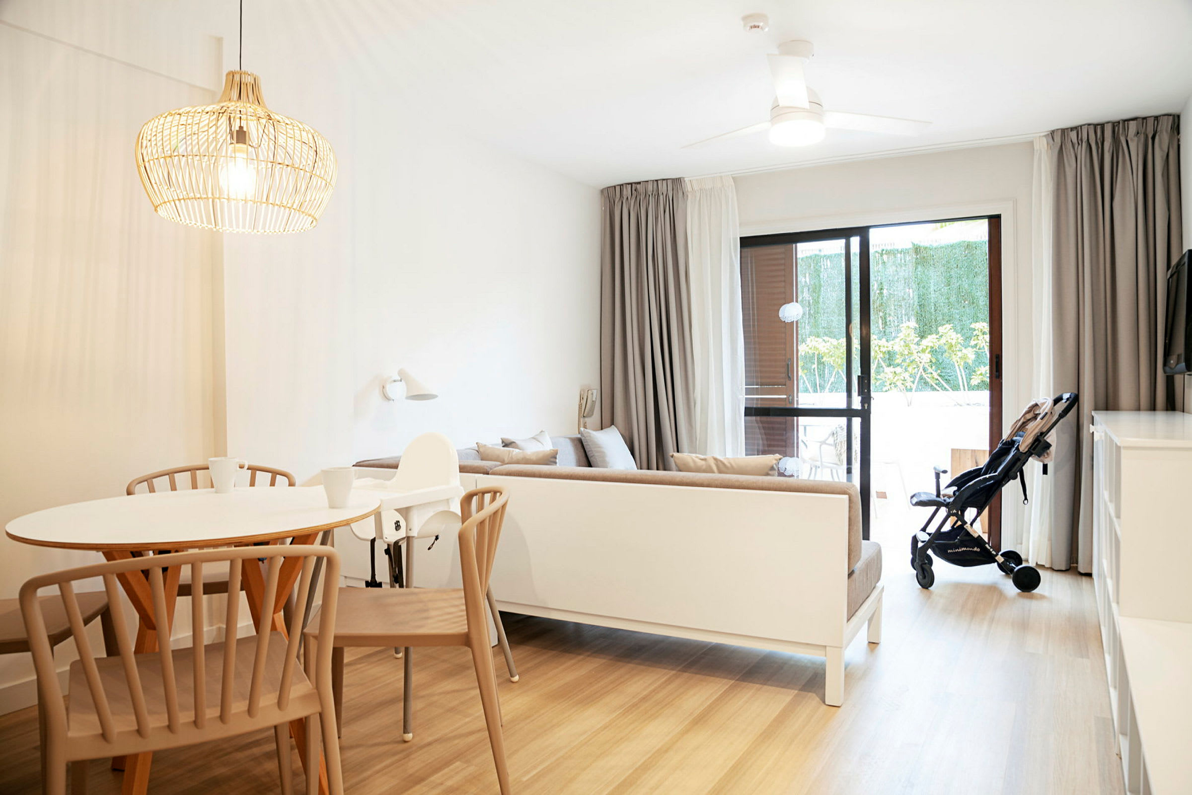 En lys og moderne indrettet stue med et spisebord, en sofa og en klapvogn ved glasdøren. (AI-genereret tekst)