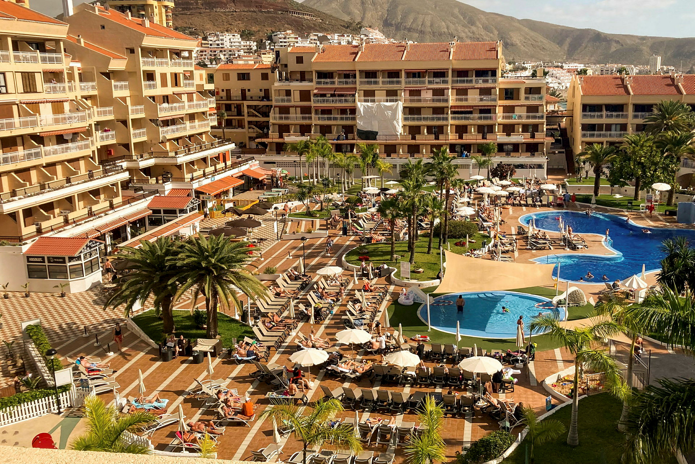 Hotelområde med swimmingpools, liggestole og bygninger i baggrunden. (AI-genereret tekst)