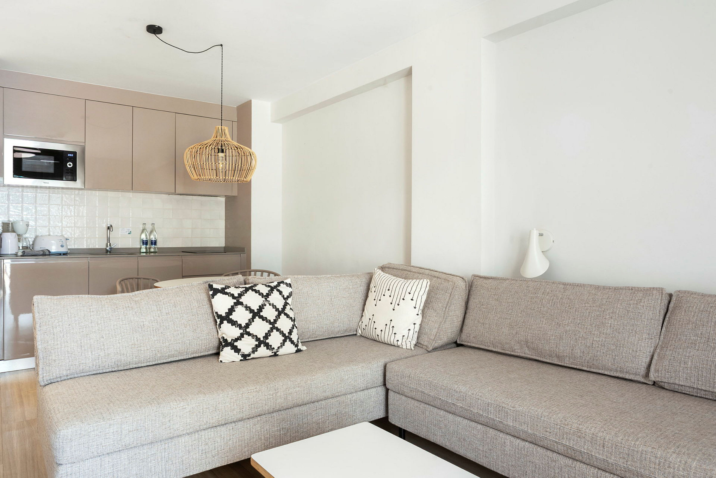 En stue med en beige sofa og køkkenområde i baggrunden. (AI-genereret tekst)
