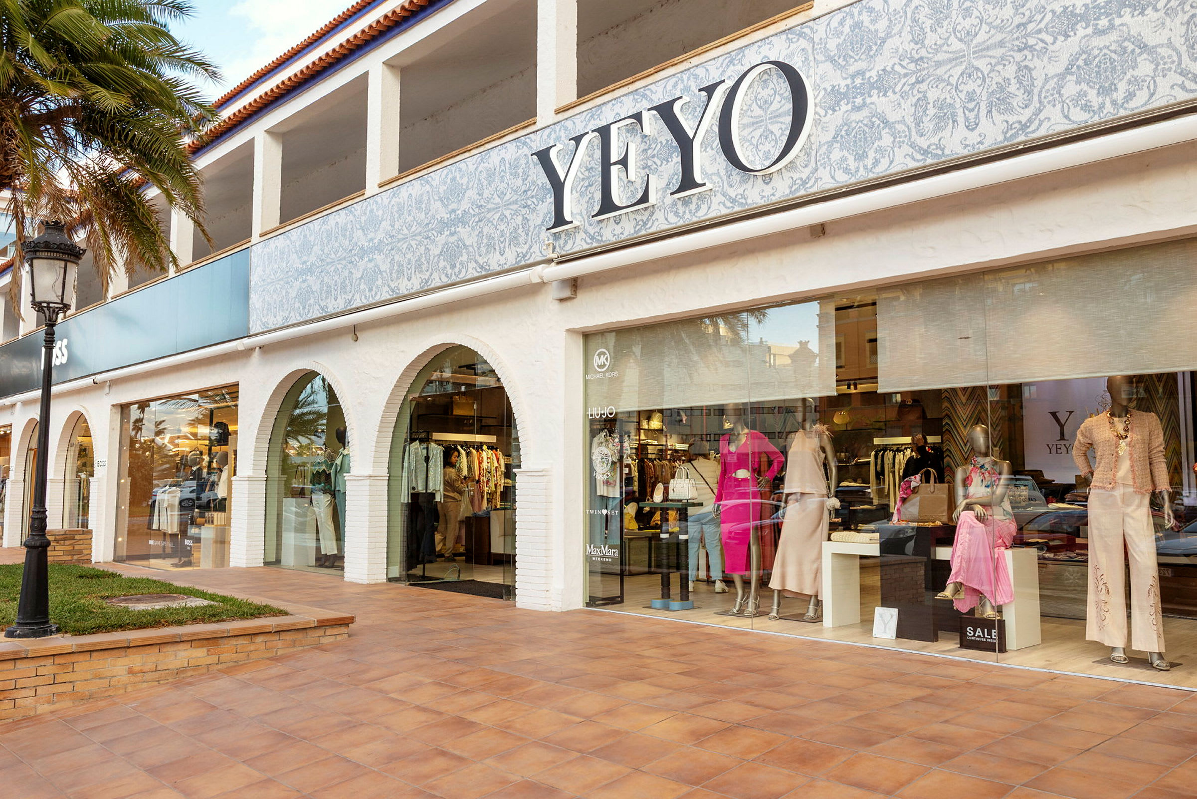 Udvendig facade af en butik med skiltet YEYO, hvor tøj og mannequinfigurer vises i vinduet. (AI-genereret tekst)