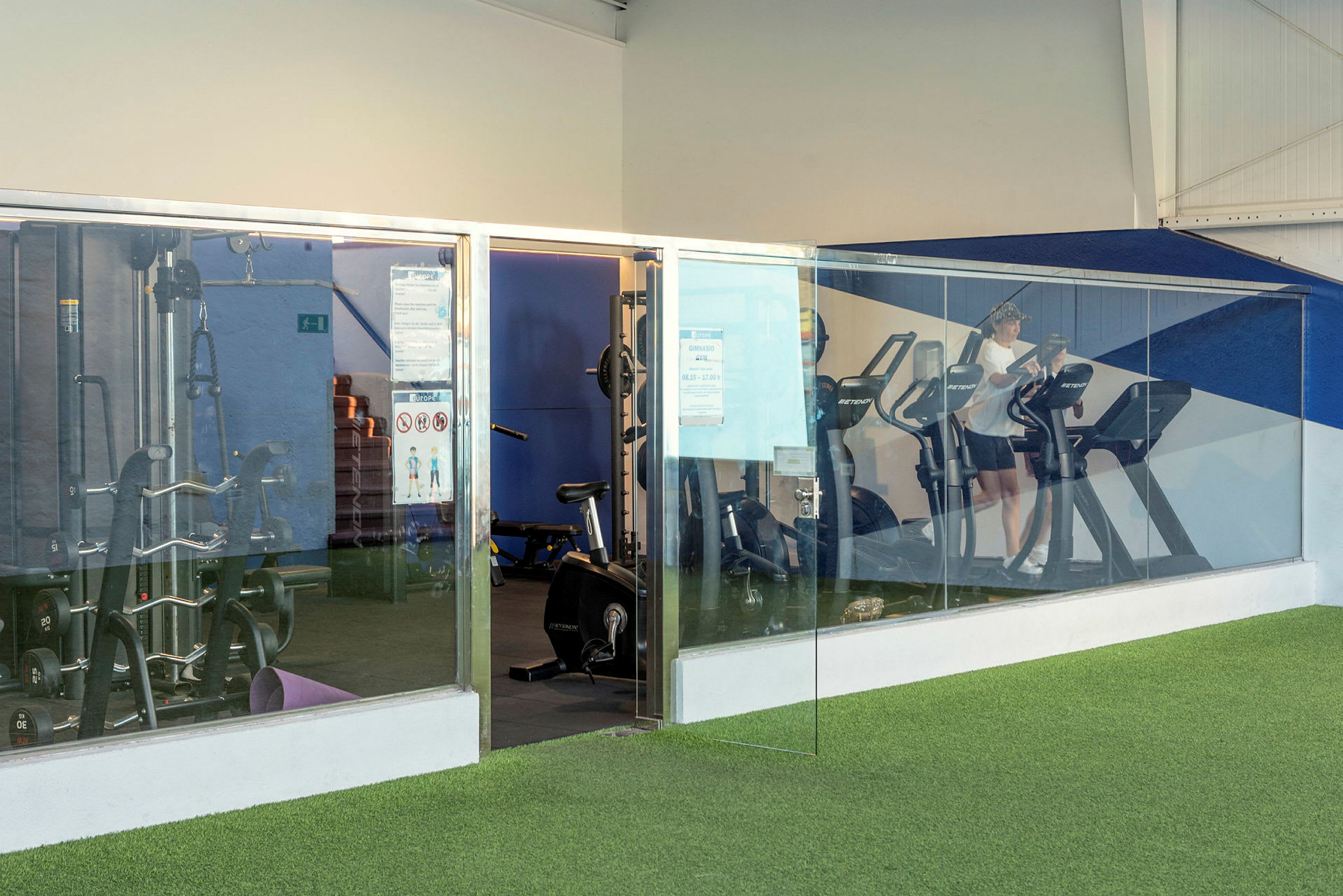 Fitnesscenter med træningsmaskiner og glasvæg. (AI-genereret tekst)