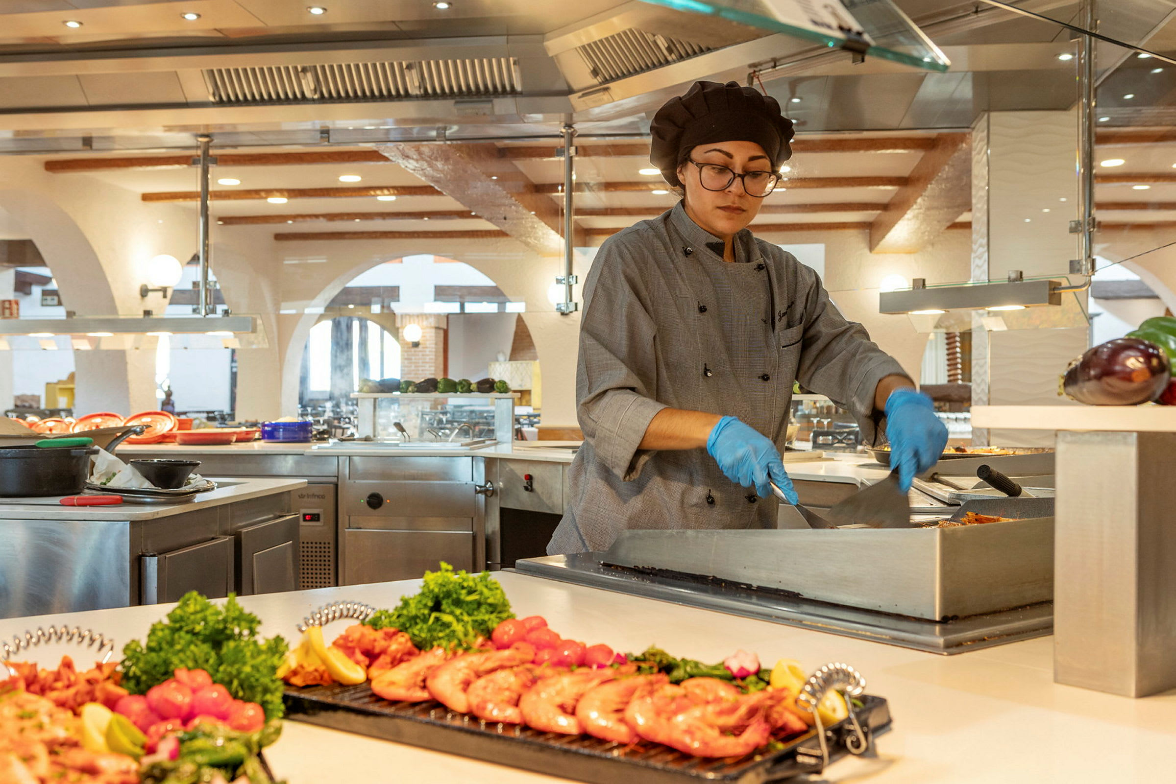 En kok tilbereder mad ved en buffetstation i et moderne køkken med bunker af friske ingredienser. (AI-genereret tekst)