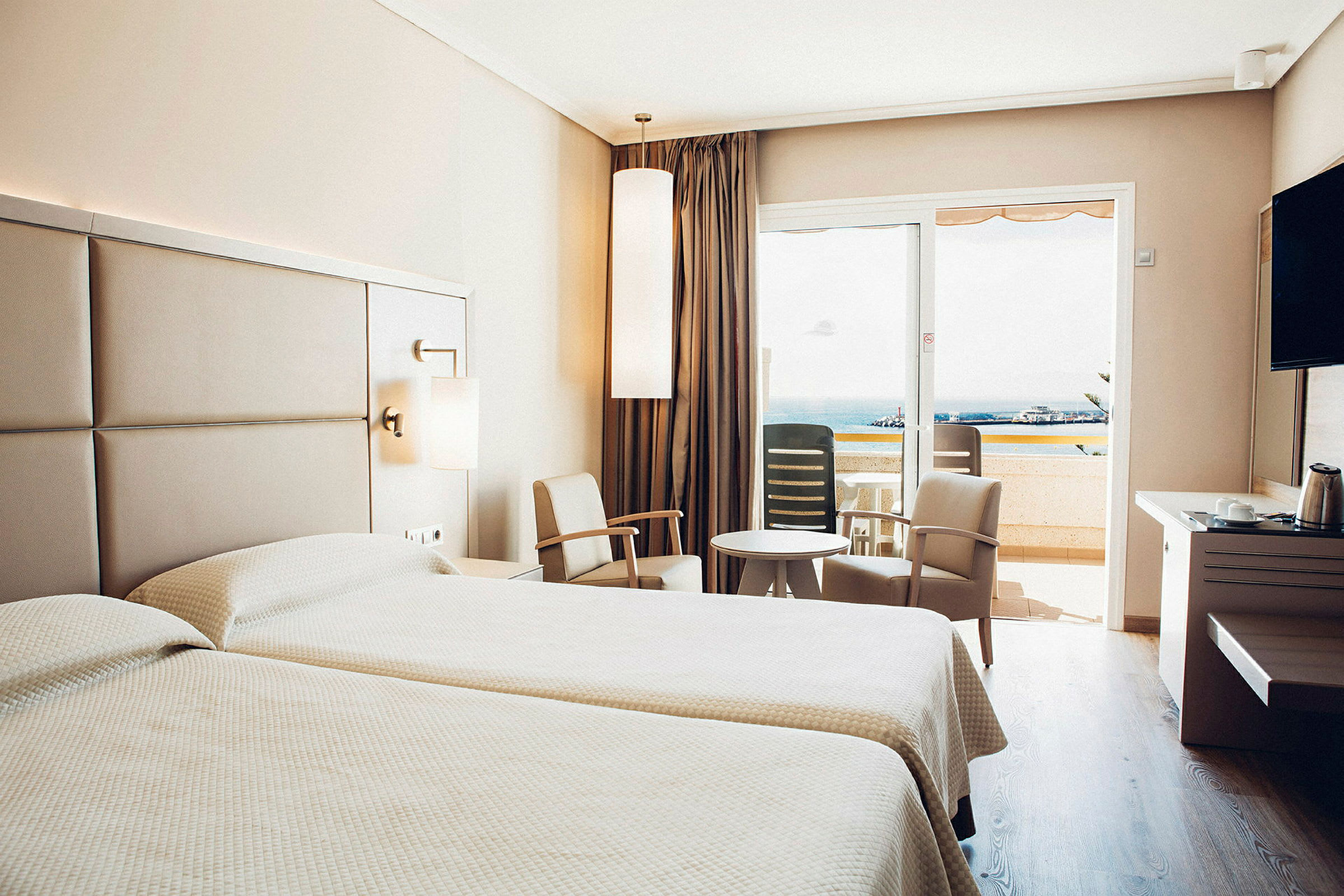 Hotelværelse med to senge, siddeområde og balkon med udsigt. (AI-genereret tekst)