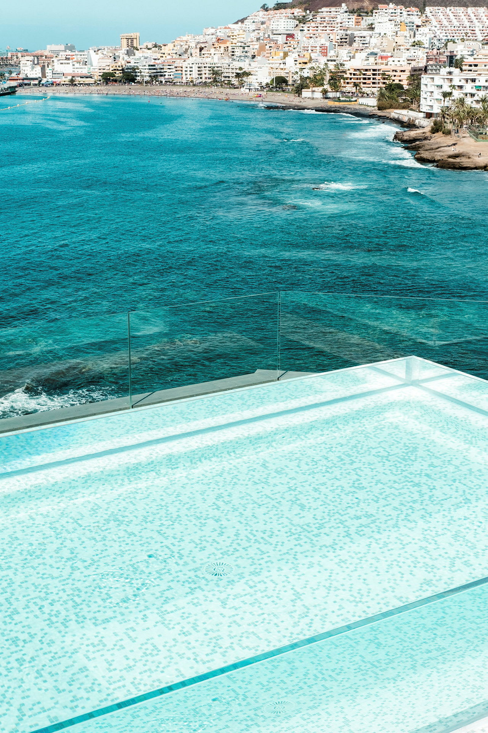 En moderne infinitypool med udsigt over havet og en bystrand. (AI-genereret tekst)