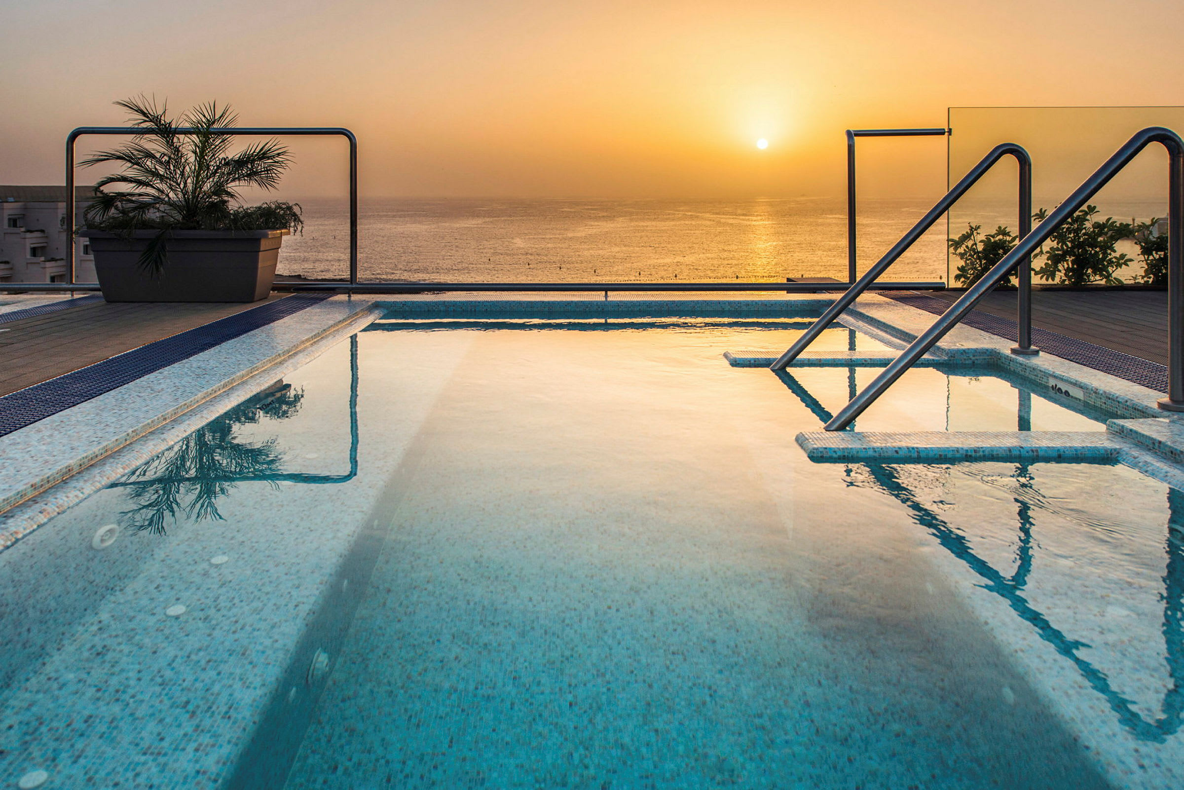 Udsigt over en pool ved solnedgang med havet i baggrunden. (AI-genereret tekst)
