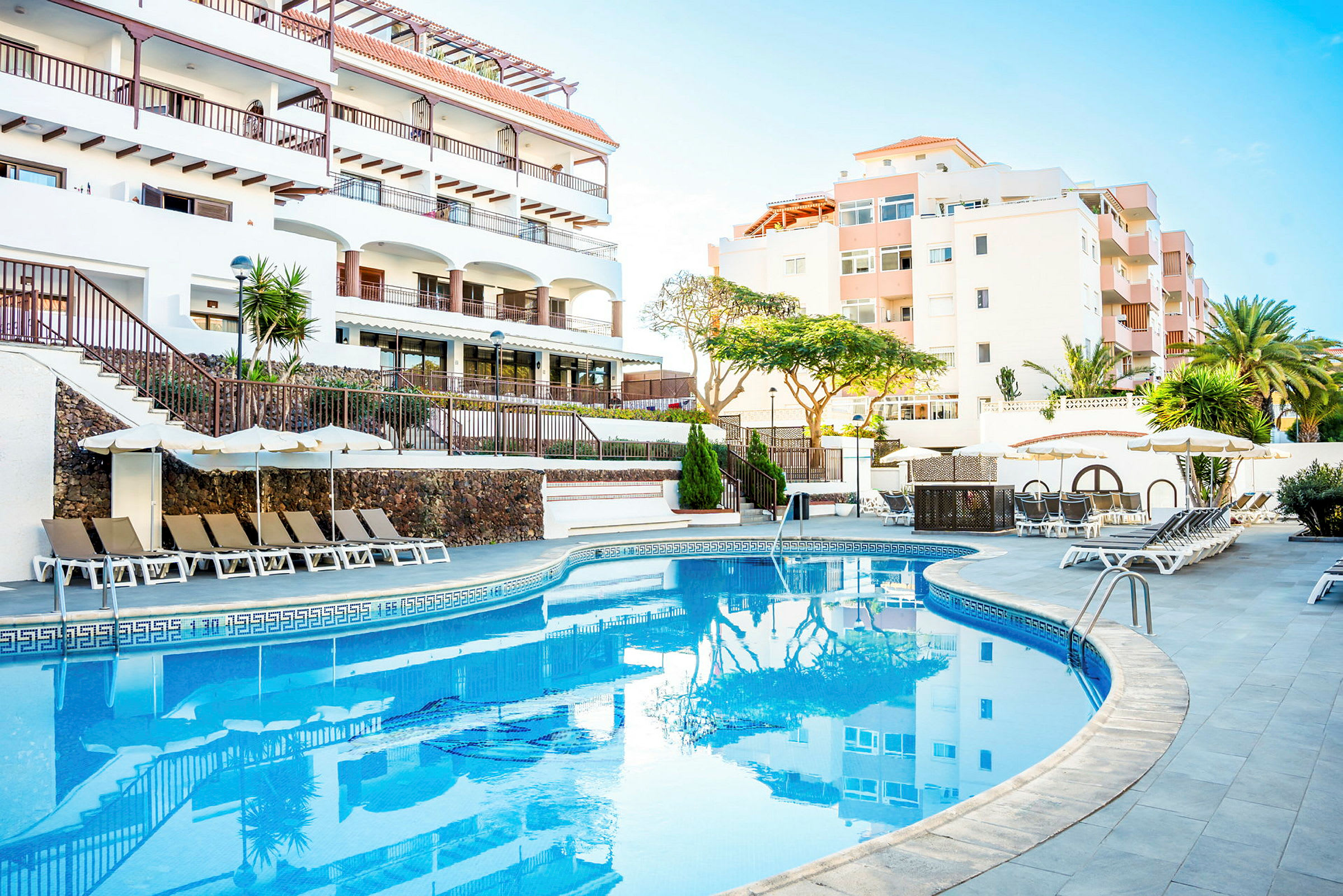 Udendørs pool med liggestole og parasoller ved et hotel. (AI-genereret tekst)