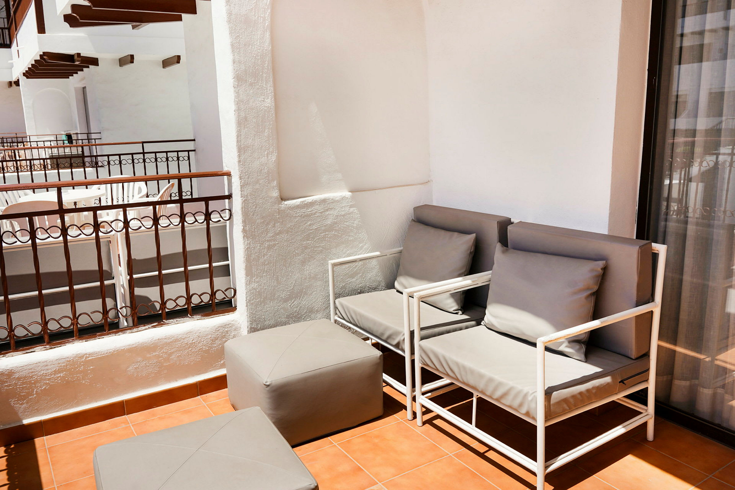 En terrasse med to grå sidemøbler og en matchende fodskammel på et terrakottaflisegulv. (AI-genereret tekst)