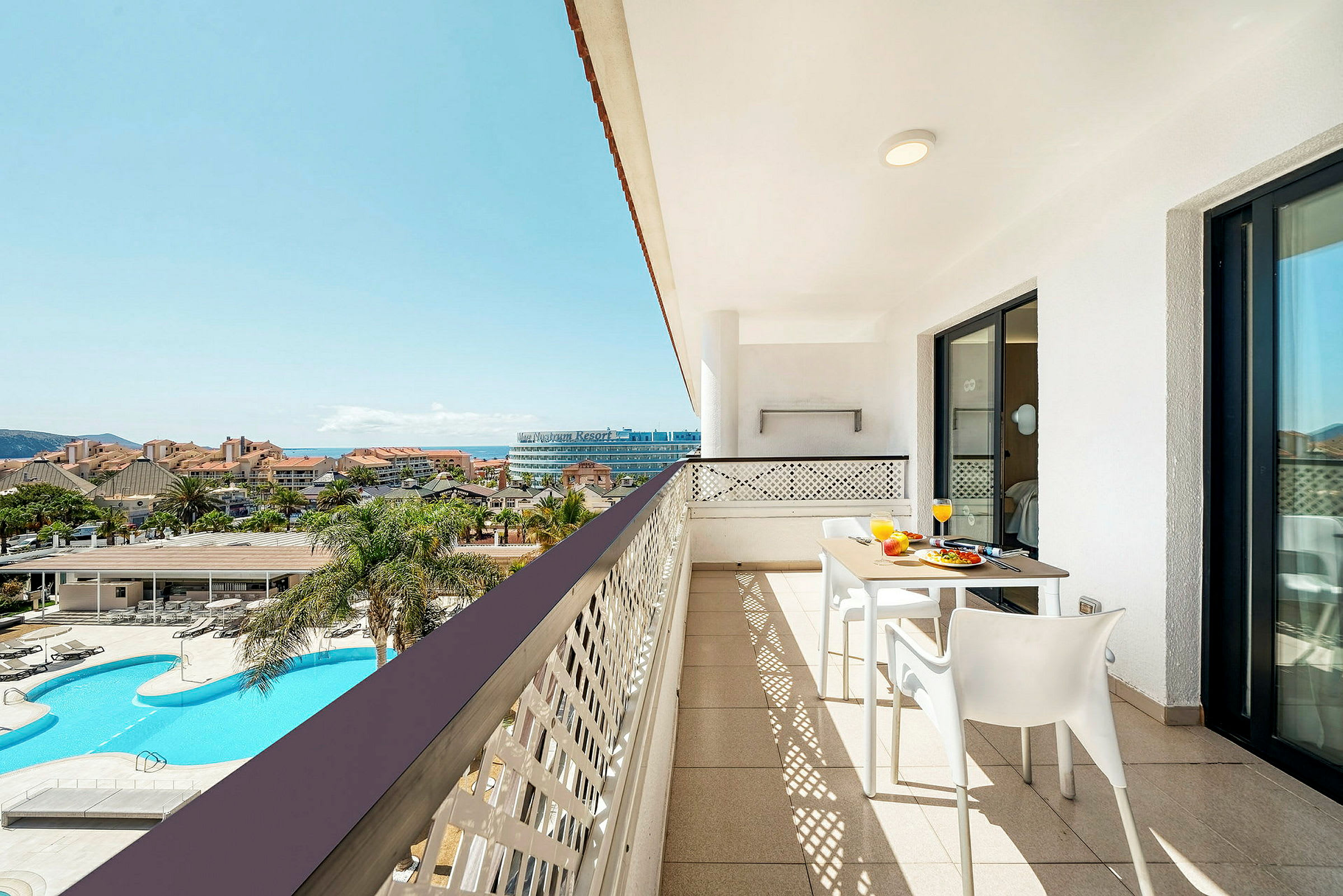 En balkon med udsigt over et poolområde og en resort. (AI-genereret tekst)