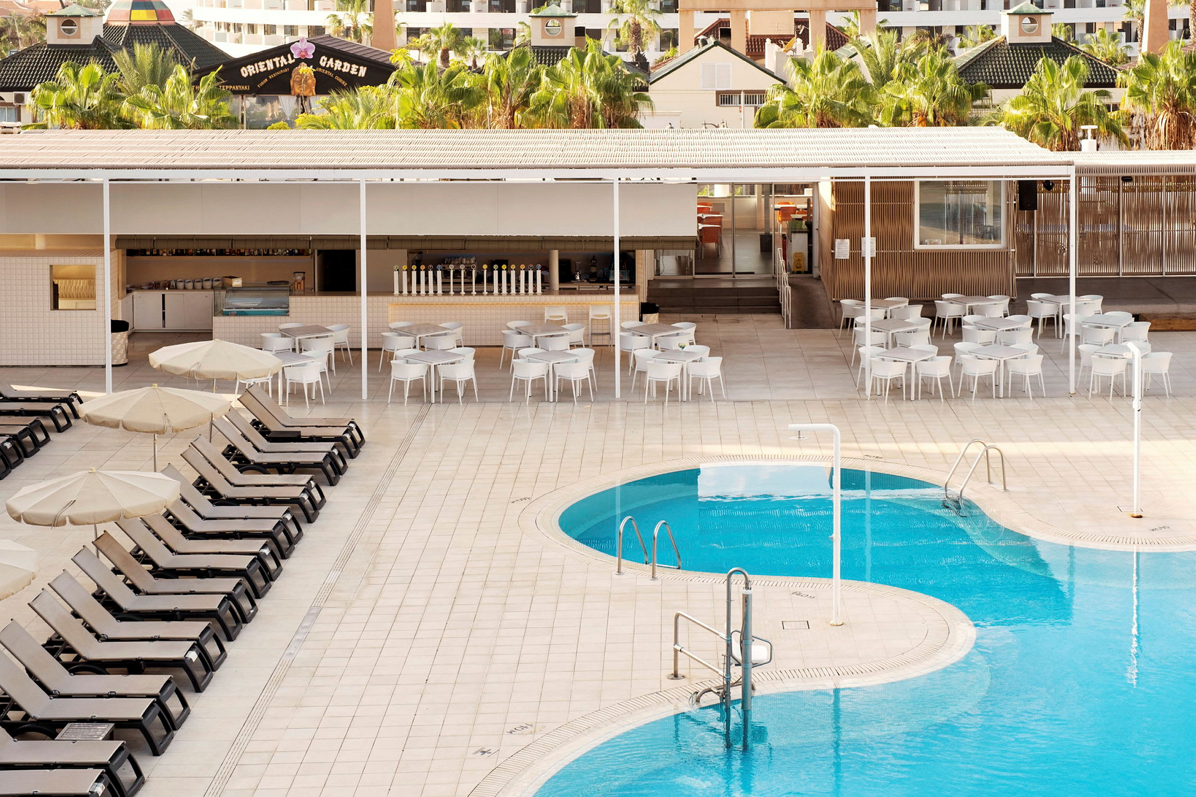 Billede af en pool med liggestole og parasoller i forgrunden samt en bar og siddepladser i baggrunden. (AI-genereret tekst)