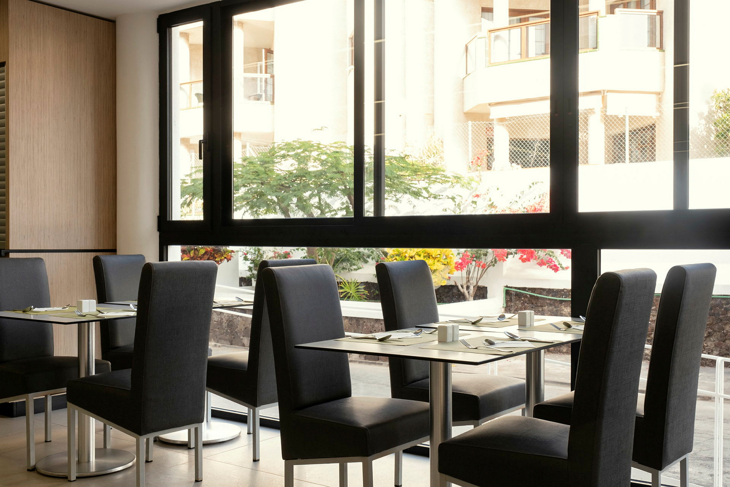 En restaurant med borde og stole, med udsigt til en gårdsplads gennem en stor glasrude. (AI-genereret tekst)