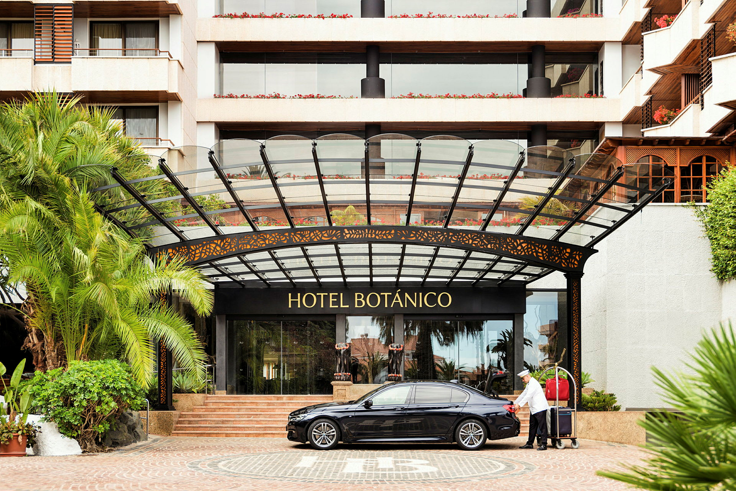 Indgangen til Hotel Botánico med en bil og en bagagevogn. (AI-genereret tekst)