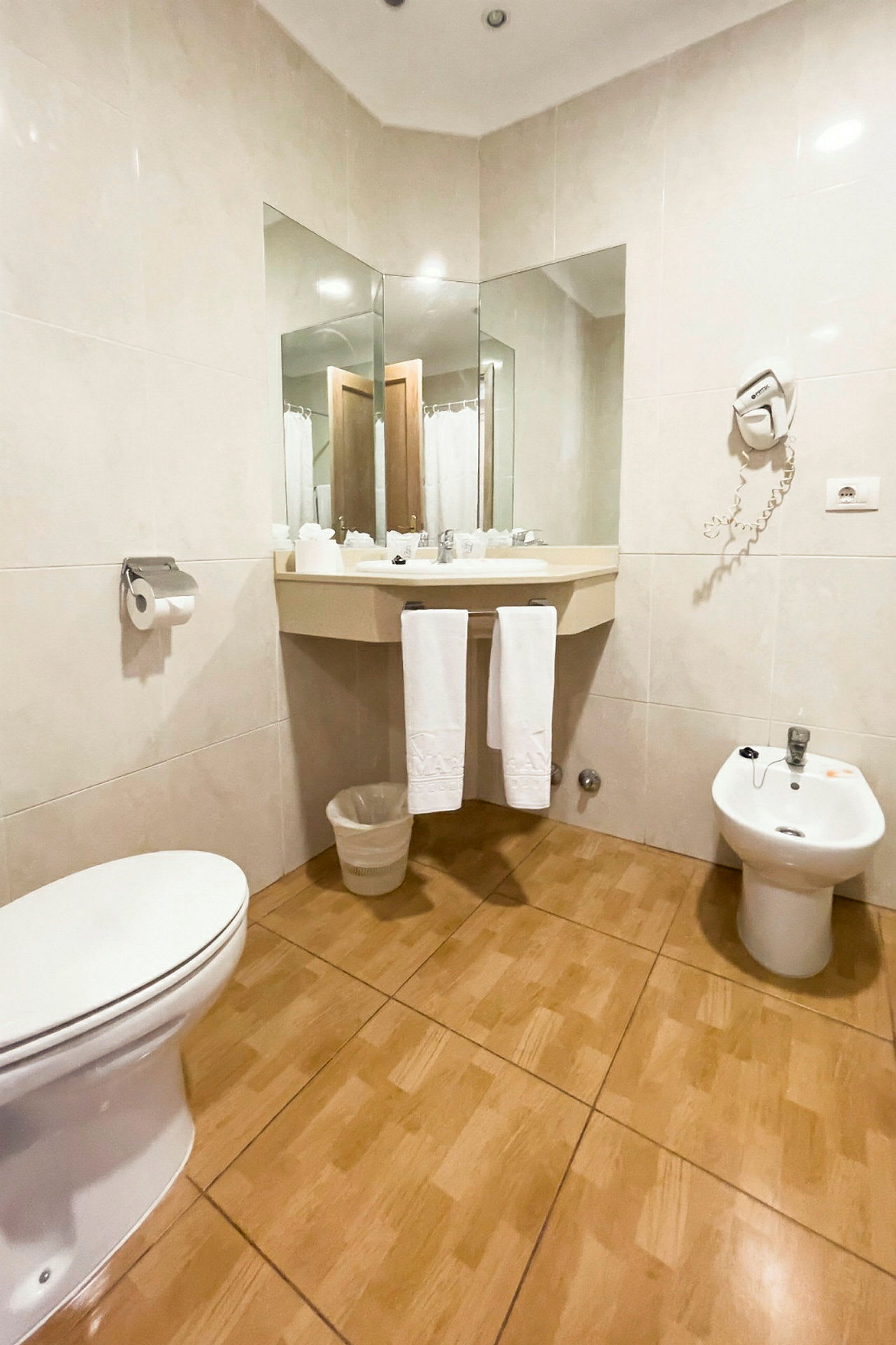 Badeværelse med toilet, bidet, håndvask med spejl og håndklæder. (AI-genereret tekst)