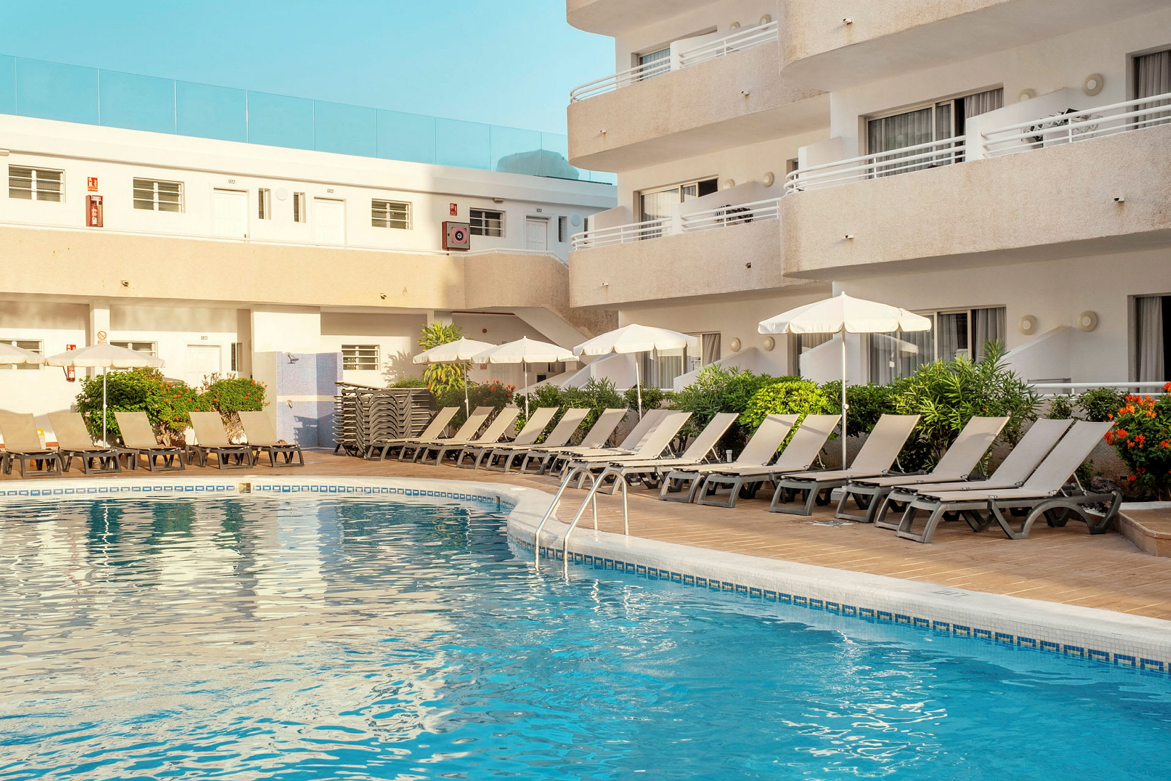 Udendørs swimmingpool med liggestole og parasoller ved et hotel. (AI-genereret tekst)